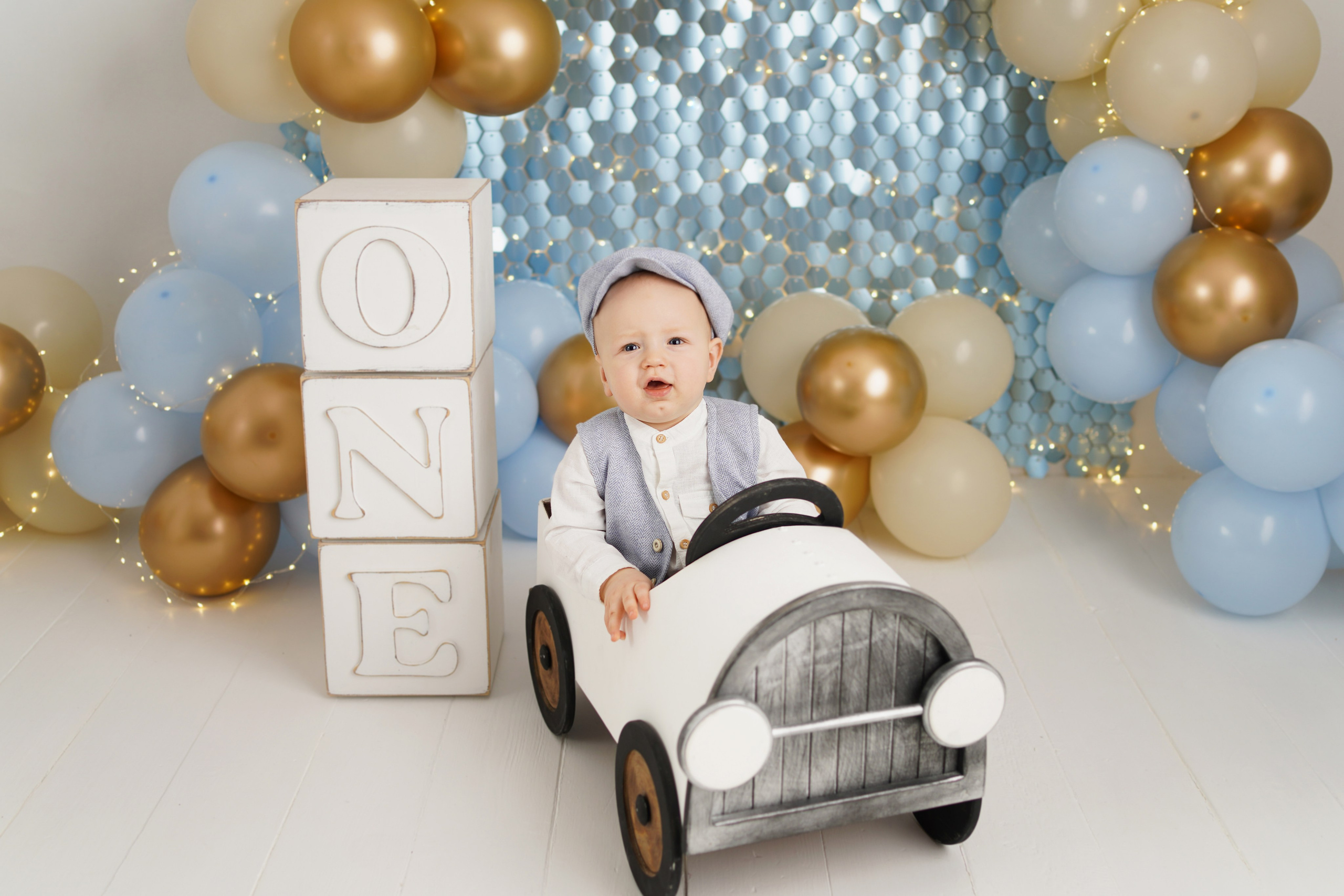 На фотосессии Первый годик малыш сидит  в машинке , рядом большие кубики год.