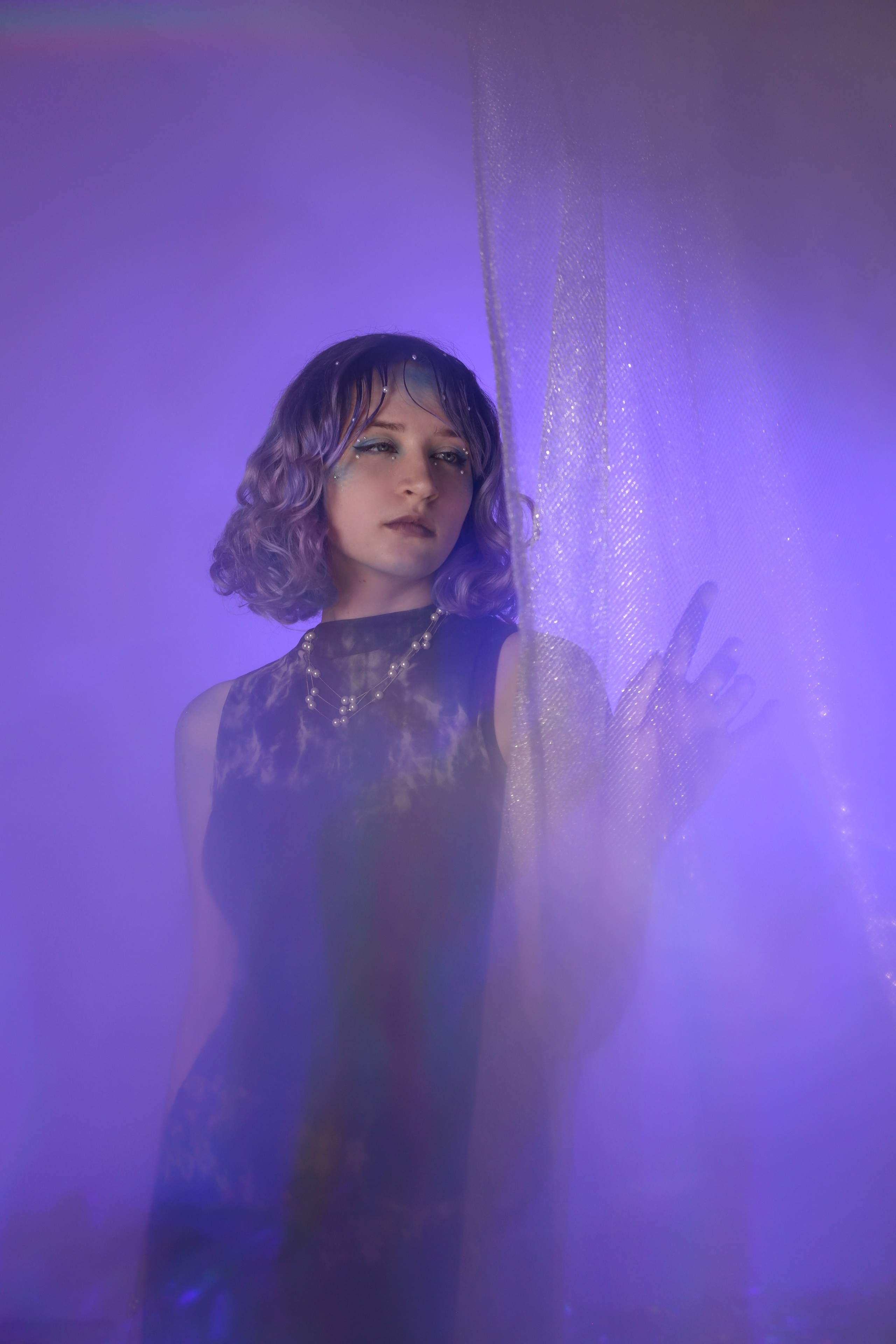 Творческая фотосессия «Ундина»: девушка в черном платье стоит у занавески в фиолетовом свете