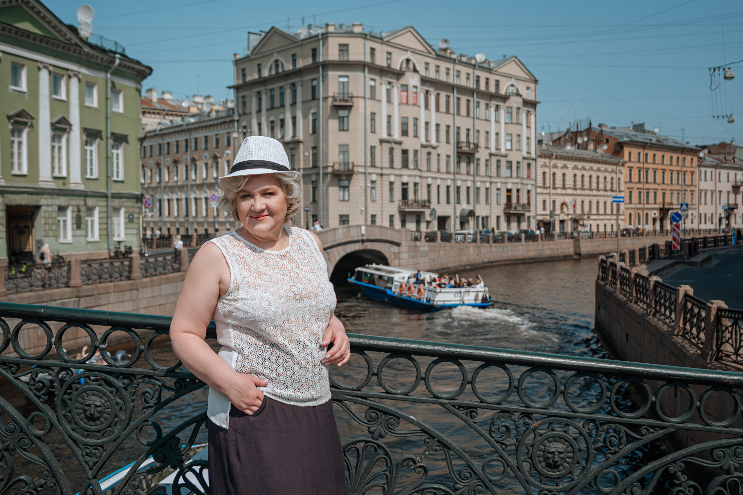 Счастливая женщина в возрасте в стильной шляпке, прогуливающаяся по Санкт-Петербургу и наслаждающаяся теплым летним воздухом.