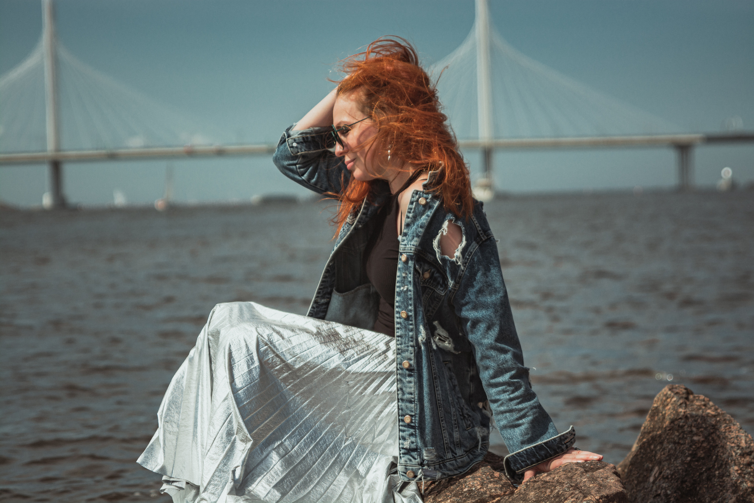 Мост на фоне, рыжеволосая девушка сидит на камнях