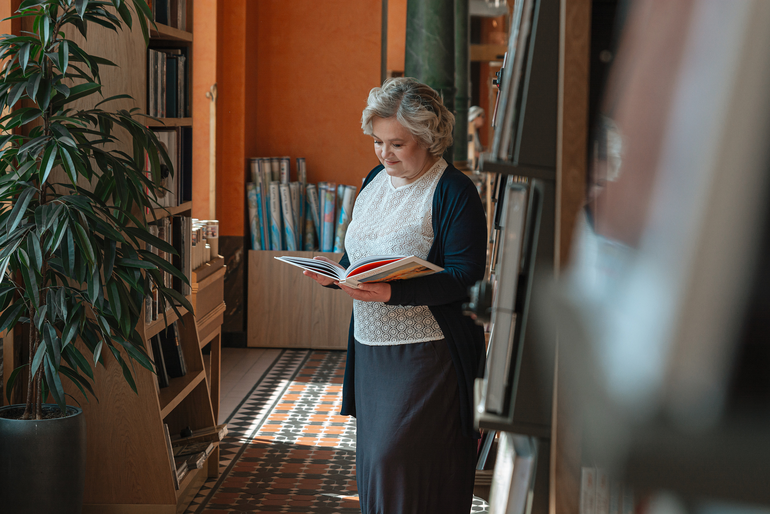  Женщина 60 лет с книгой в руках наслаждается чтением в уютном Доме Зингера в Санкт-Петербурге.