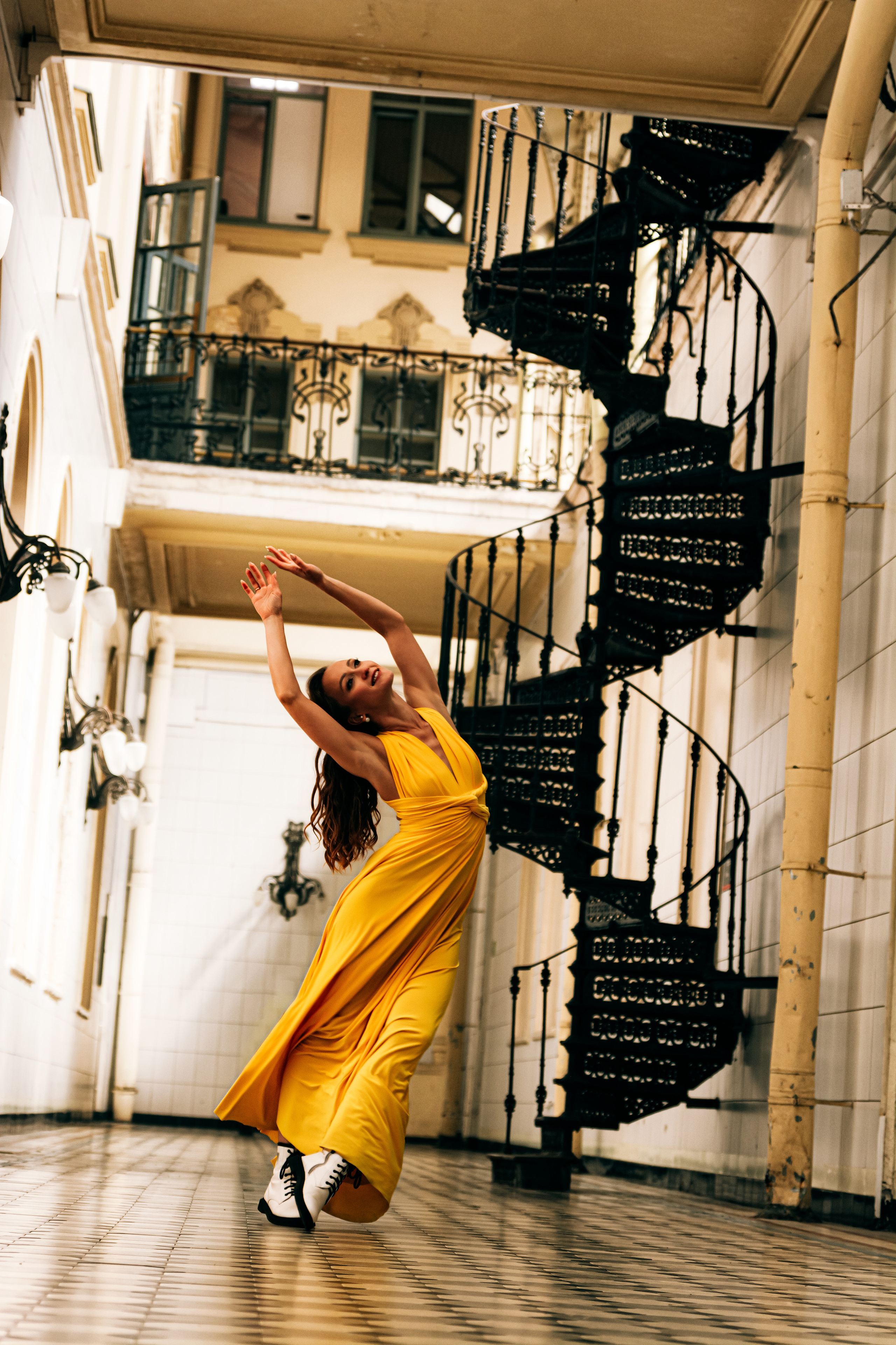 Молодая женщина, одетая в яркое желтое платье, танцует на Витебском вокзале.