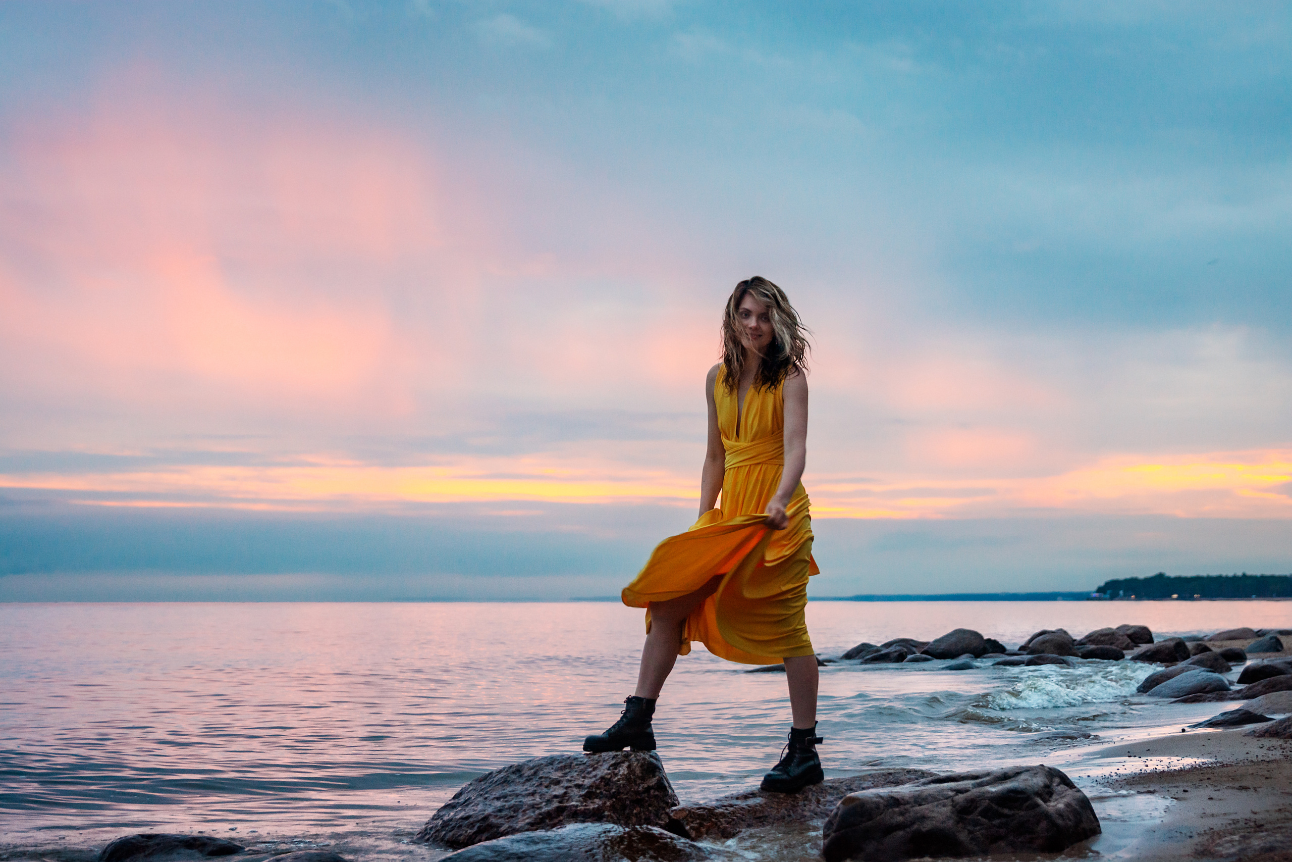 Девушка в легком розовом платье стоит на камнях в воде, окруженная природой.