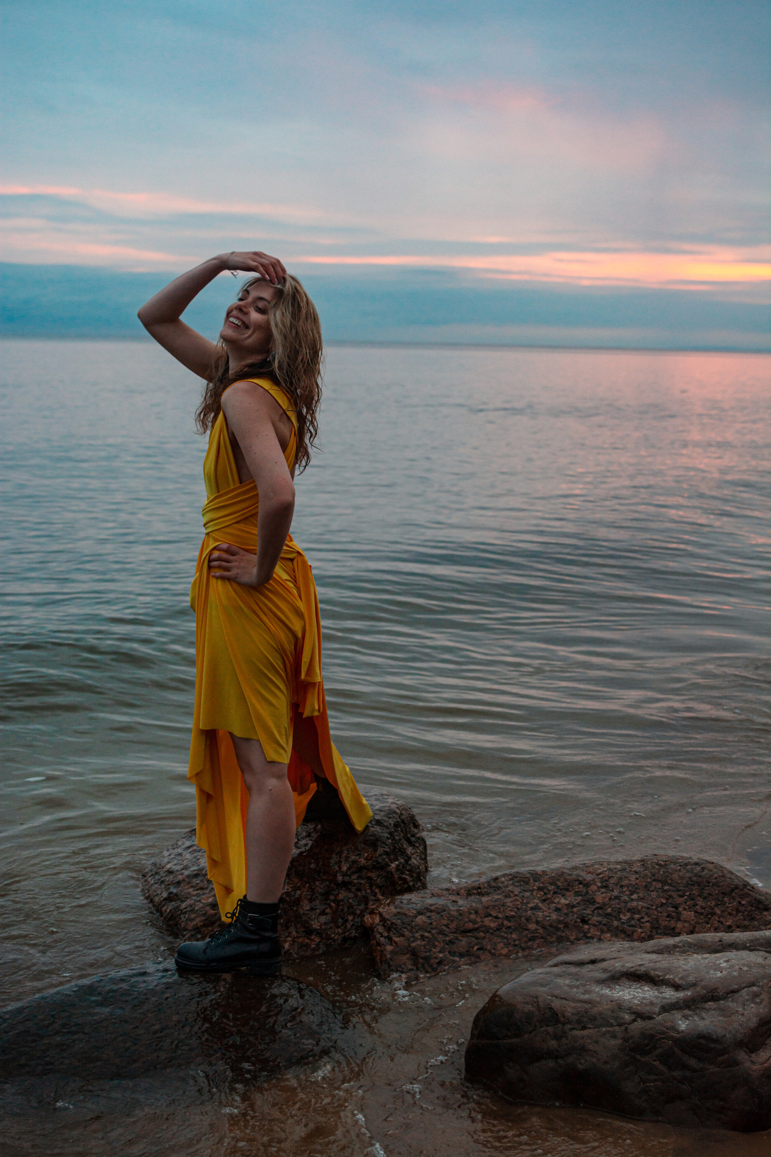  Красивая девушка в желтом платье принимает элегантные позы во время фотосессии на берегу Финского залива, где закат добавляет магии и романтики.