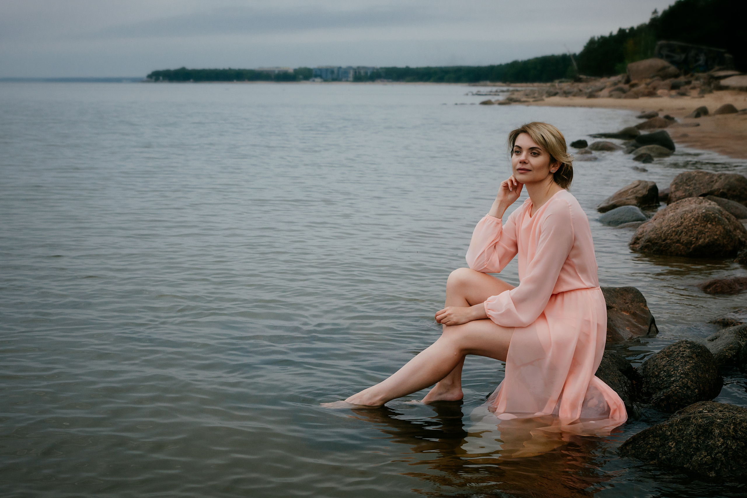 Одетая в легкое розовое платье, девушка создает гармоничное единство с окружающими ее камнями и водой.