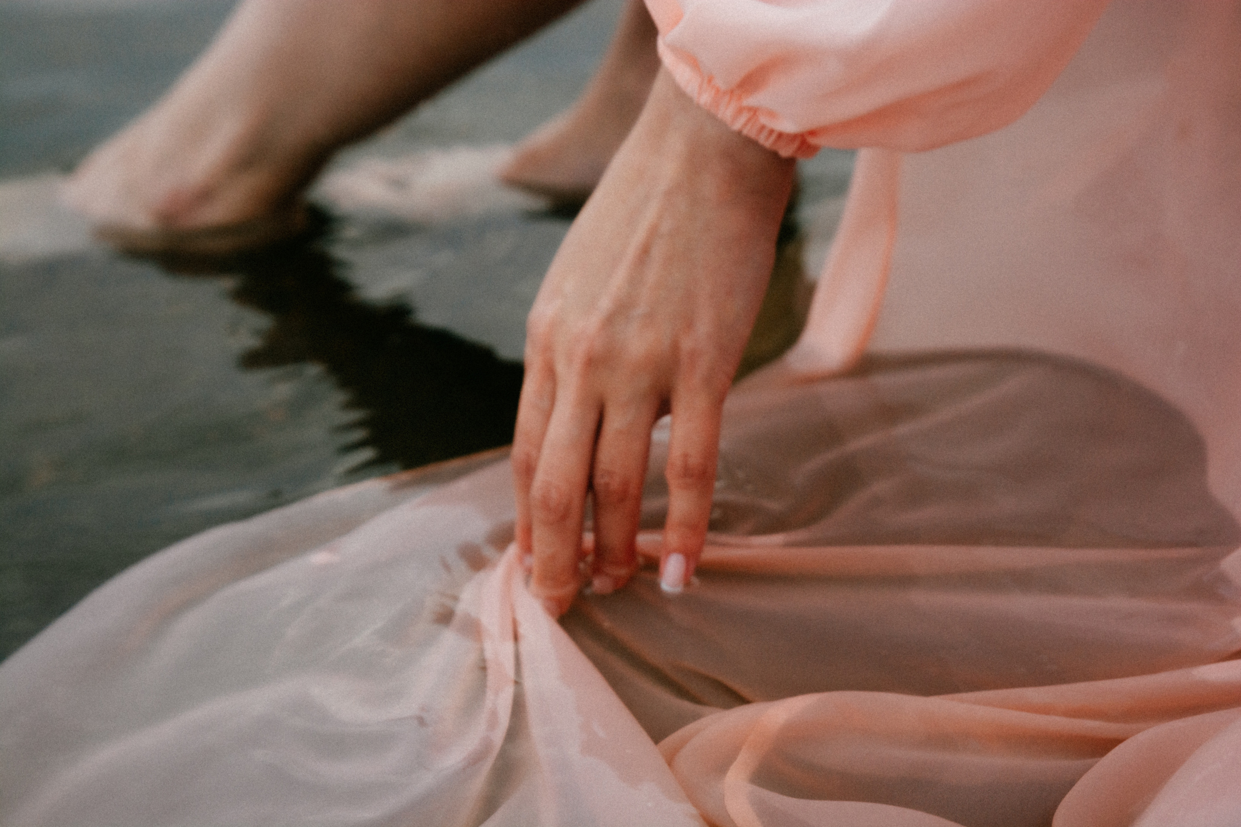 В этом фото запечатлен волшебный момент, когда девушка в розовом платье наслаждается моментом на камнях во время игры с водой