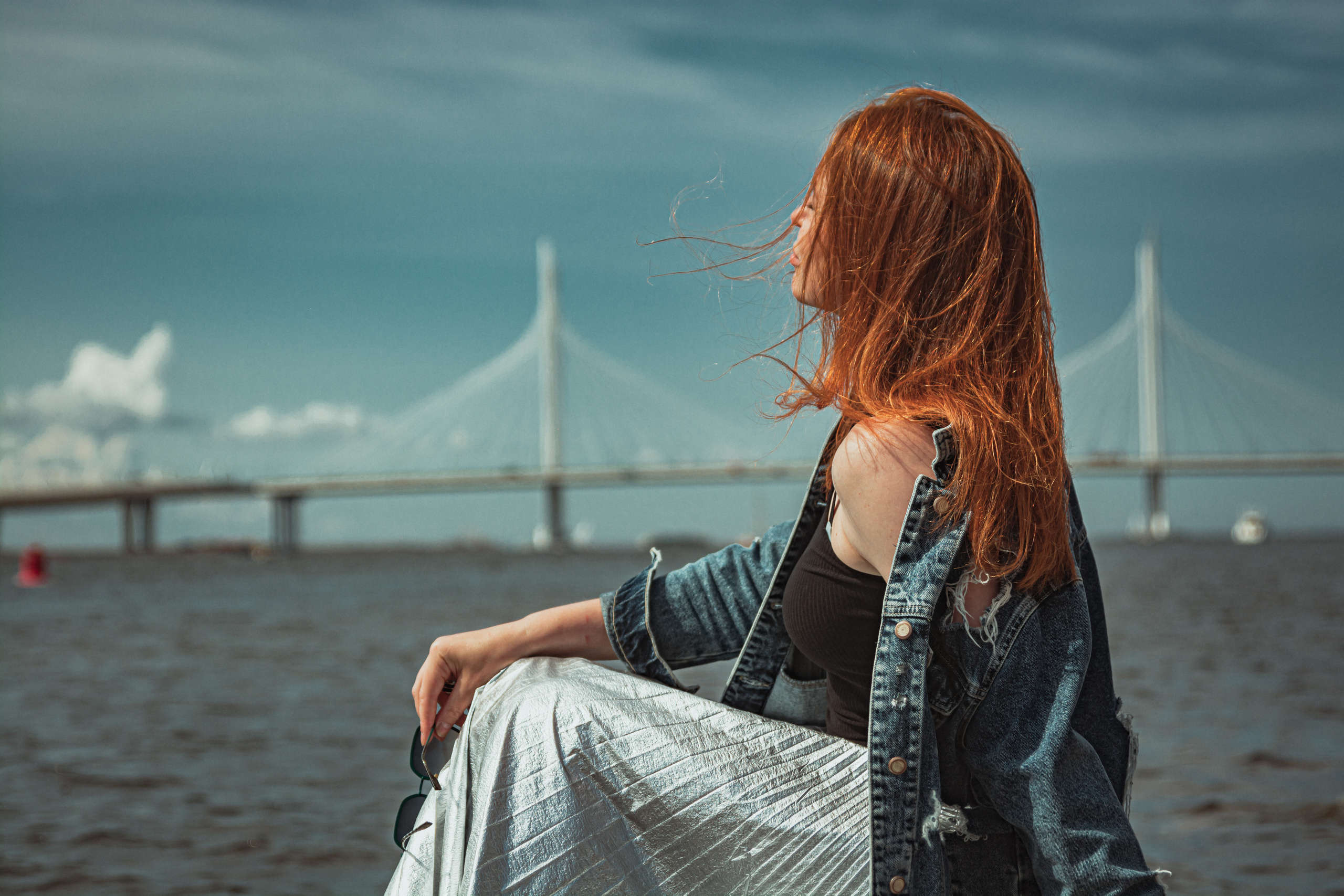 Мост на фоне, рыжеволосая девушка сидит на камнях