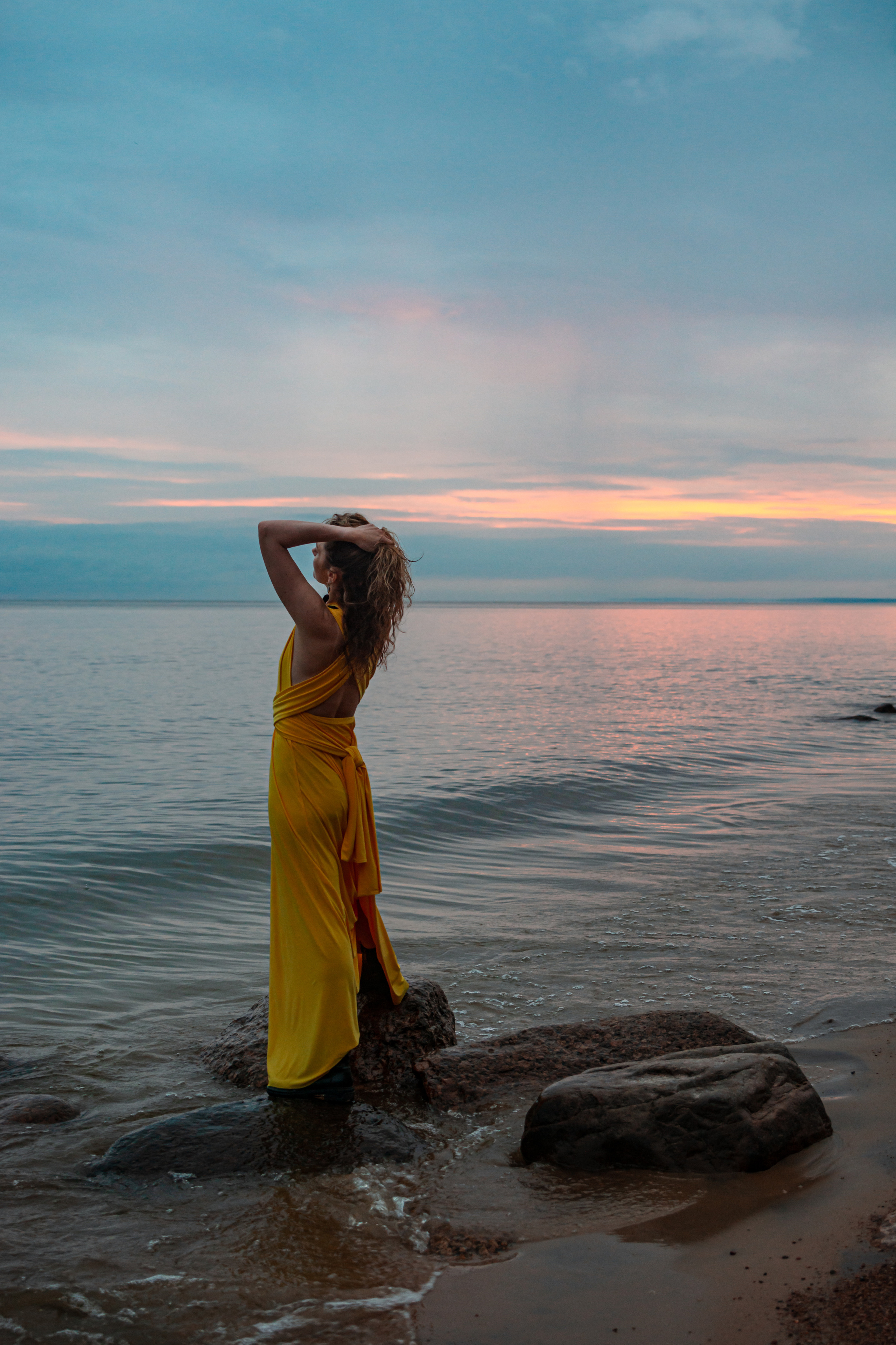 Девушка в желтом платье наслаждается красотой заката на берегу Финского залива.