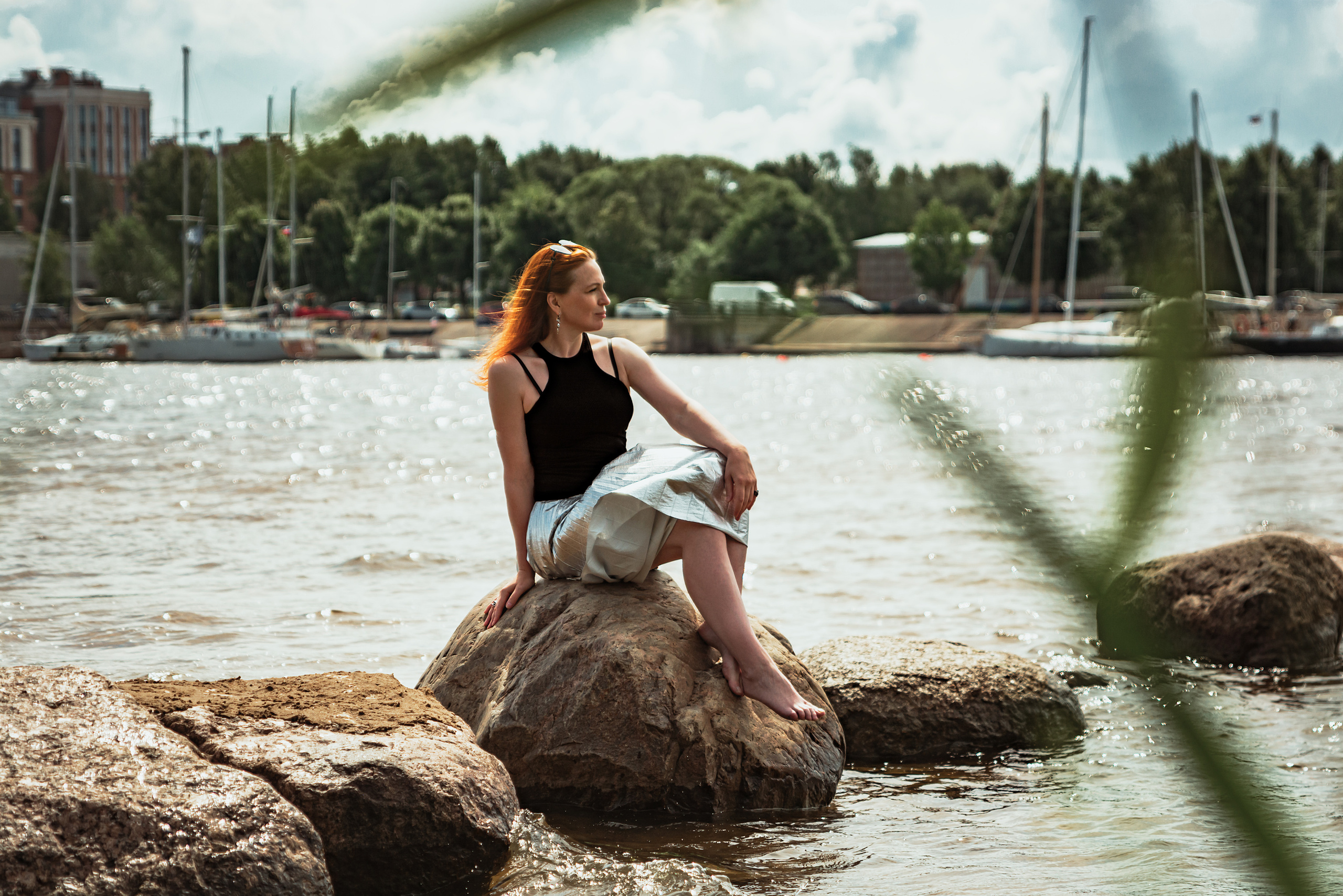 Рыжеволосая девушка сидит на камнях