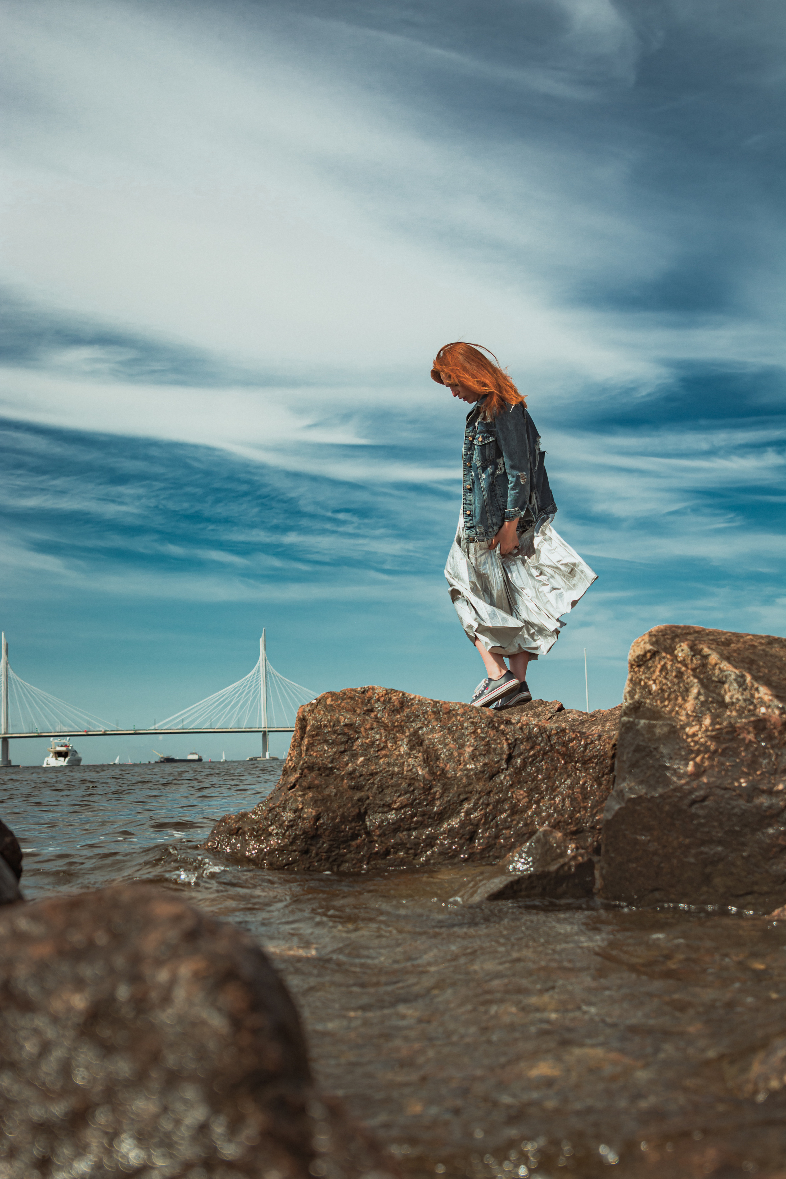 Мост на фоне, рыжеволосая девушка стоит на камнях