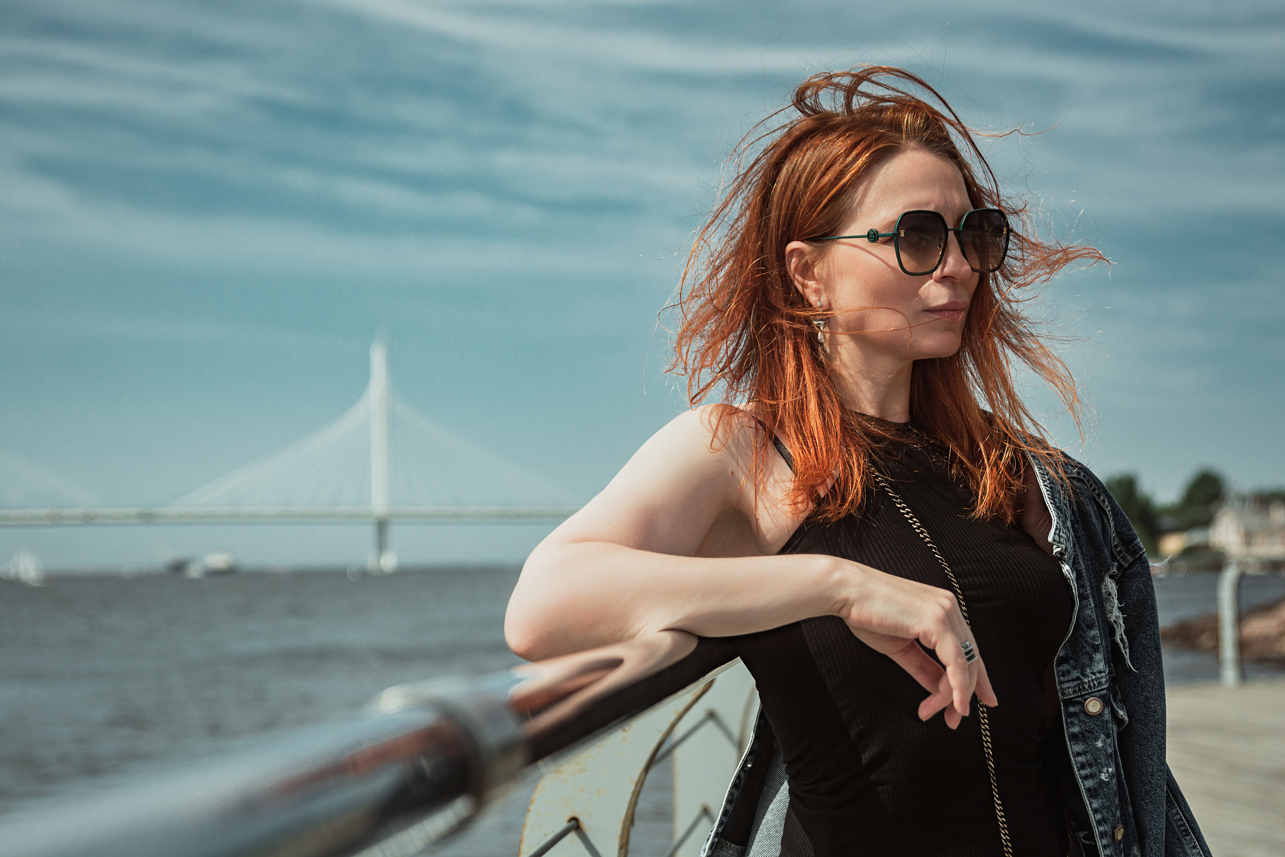 Мост на фоне, рыжеволосая девушка стоит на набережной