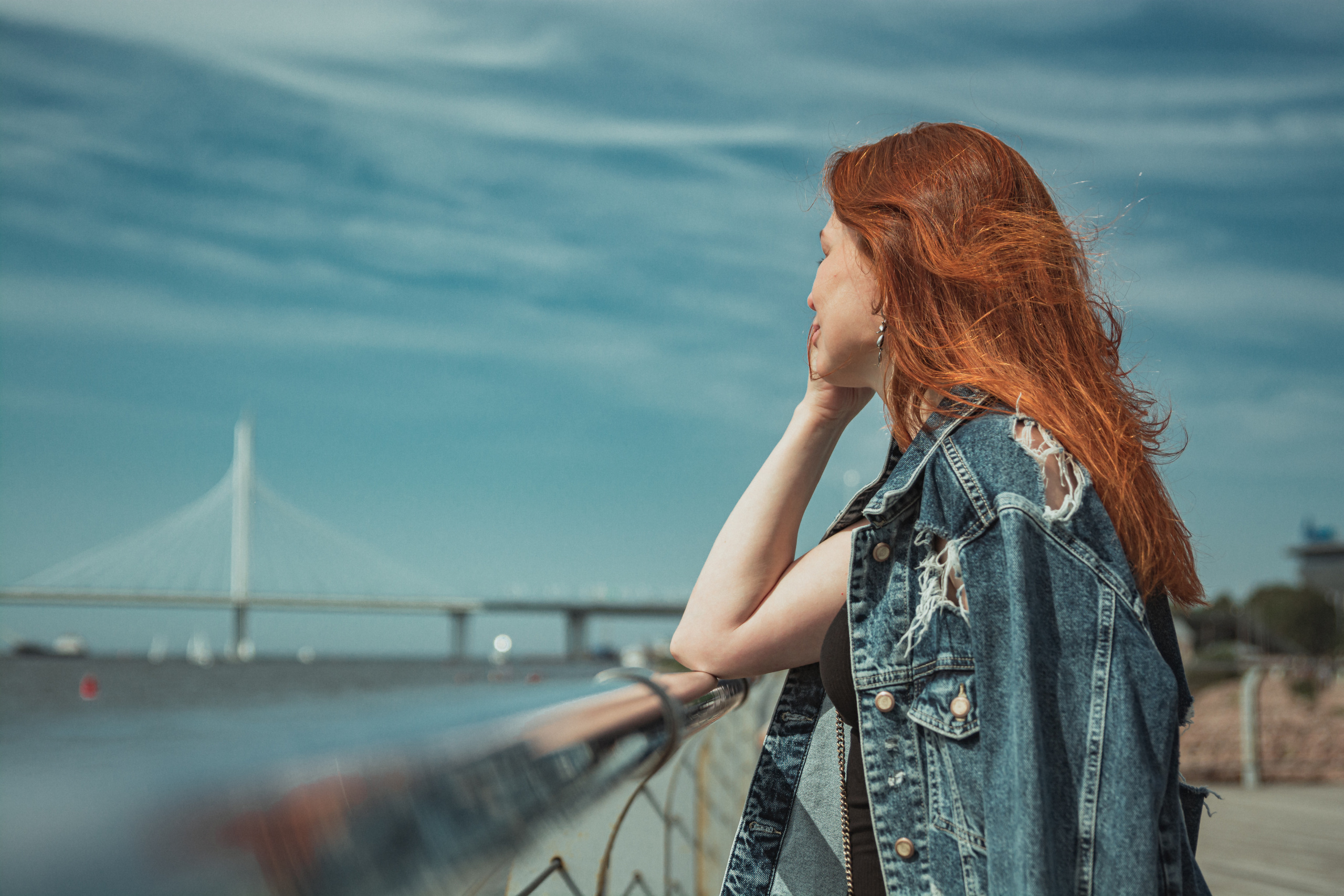 Мост на фоне, рыжеволосая девушка стоит на набережной