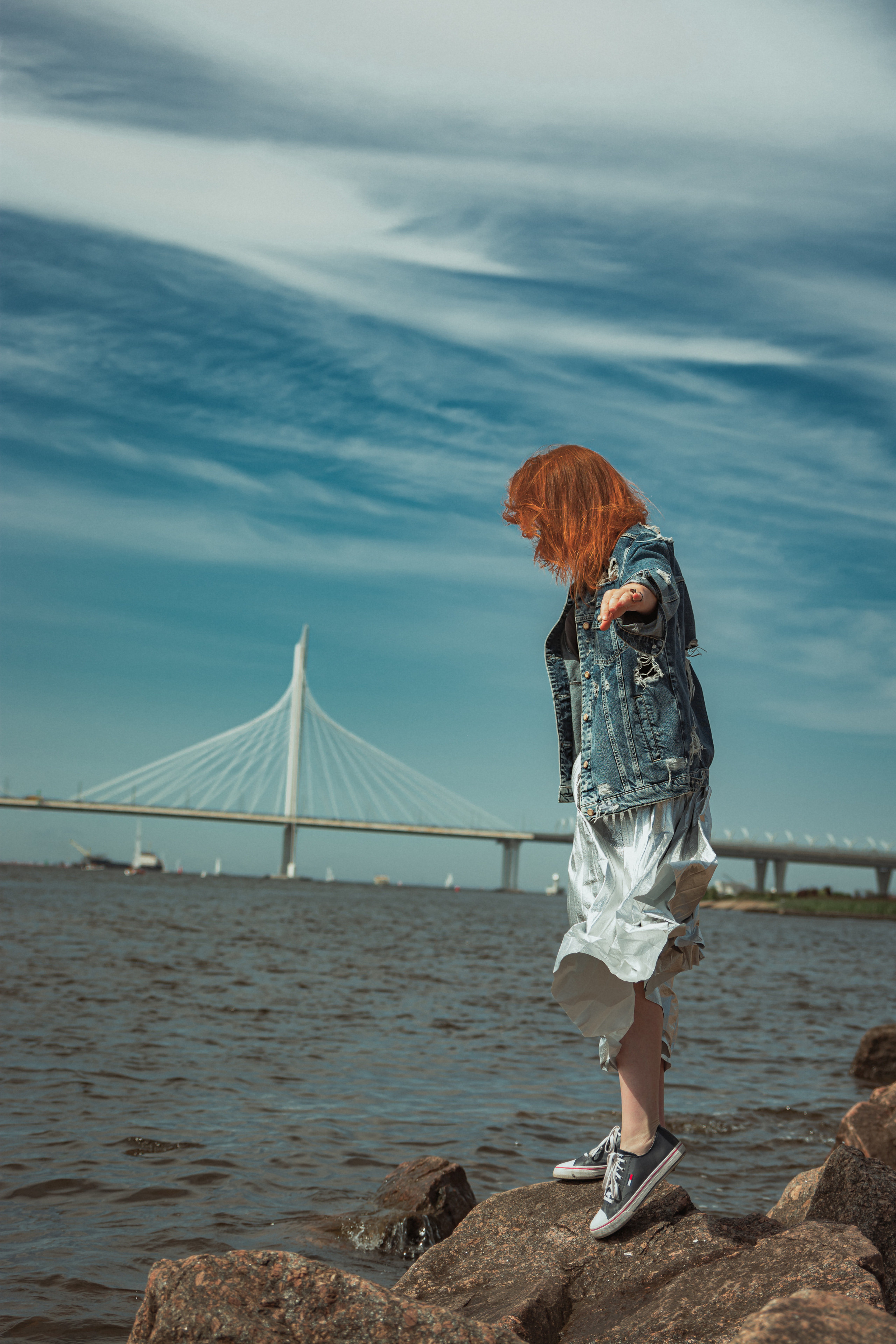 Мост на фоне, рыжеволосая девушка стоит на камнях