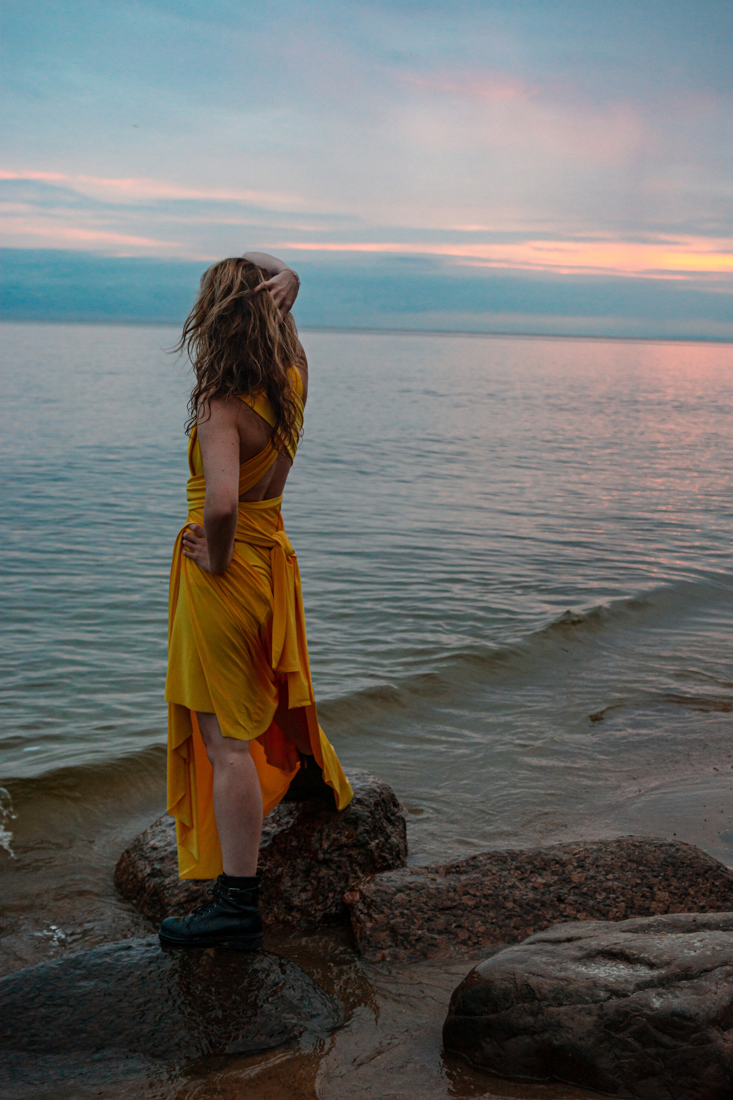 Камни Финского залива становятся идеальным фоном для фотографии, на которой девушка в желтом платье созерцает завораживающий закат.