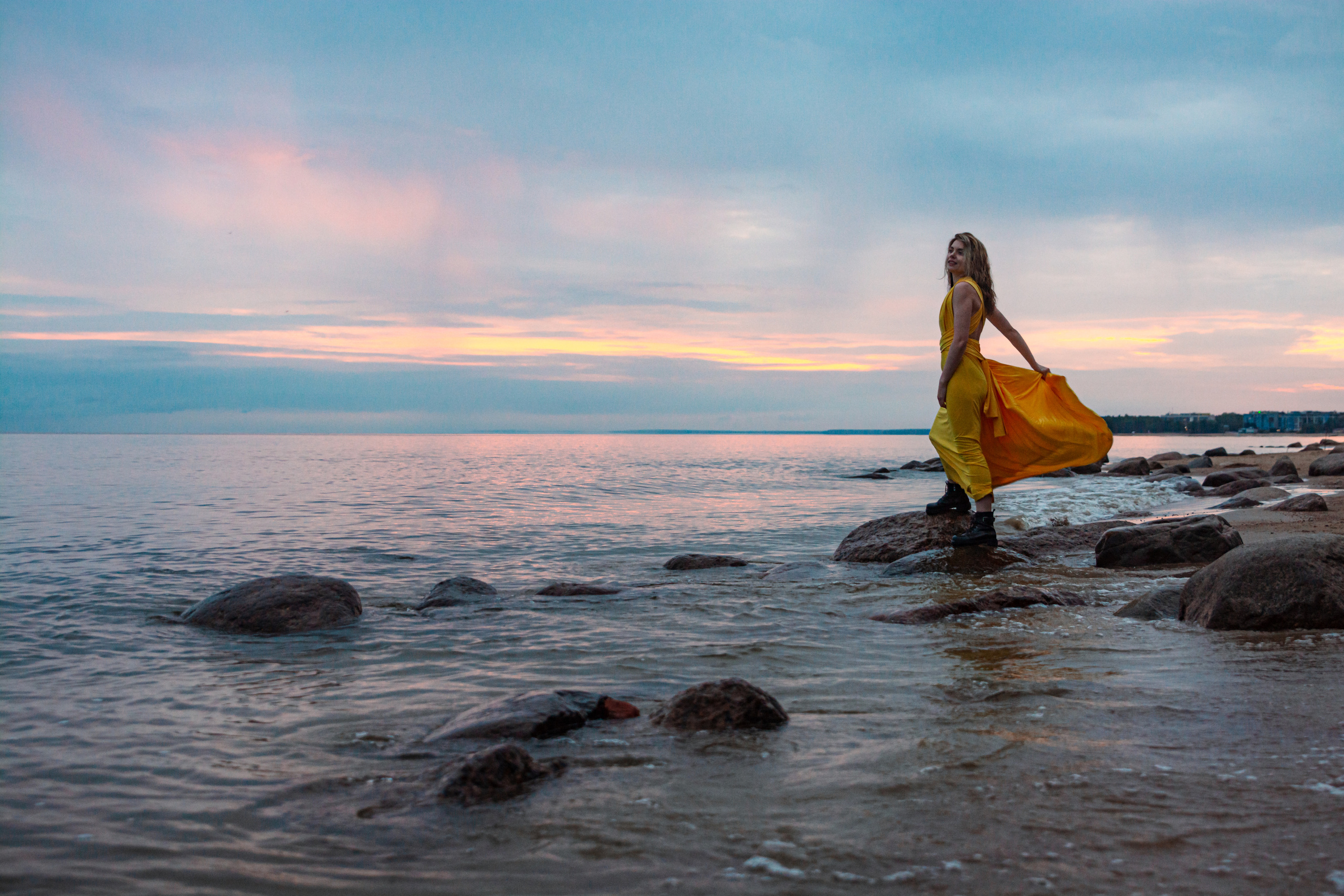 Волнующий закат Финского залива украшает фотографию, на которой танцует девушка в желтом платье, словно олицетворяя свободу и красоту природы.
