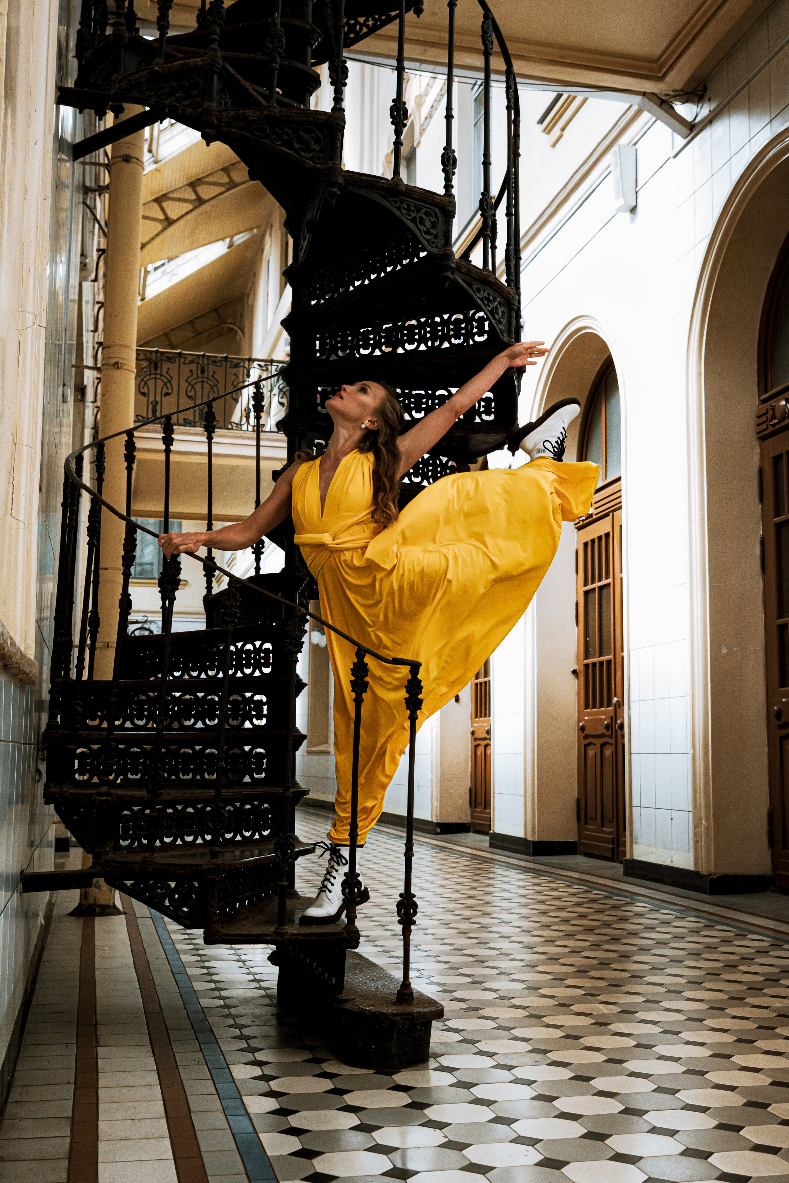 Молодая женщина, одетая в яркое желтое платье, танцует на Витебском вокзале.