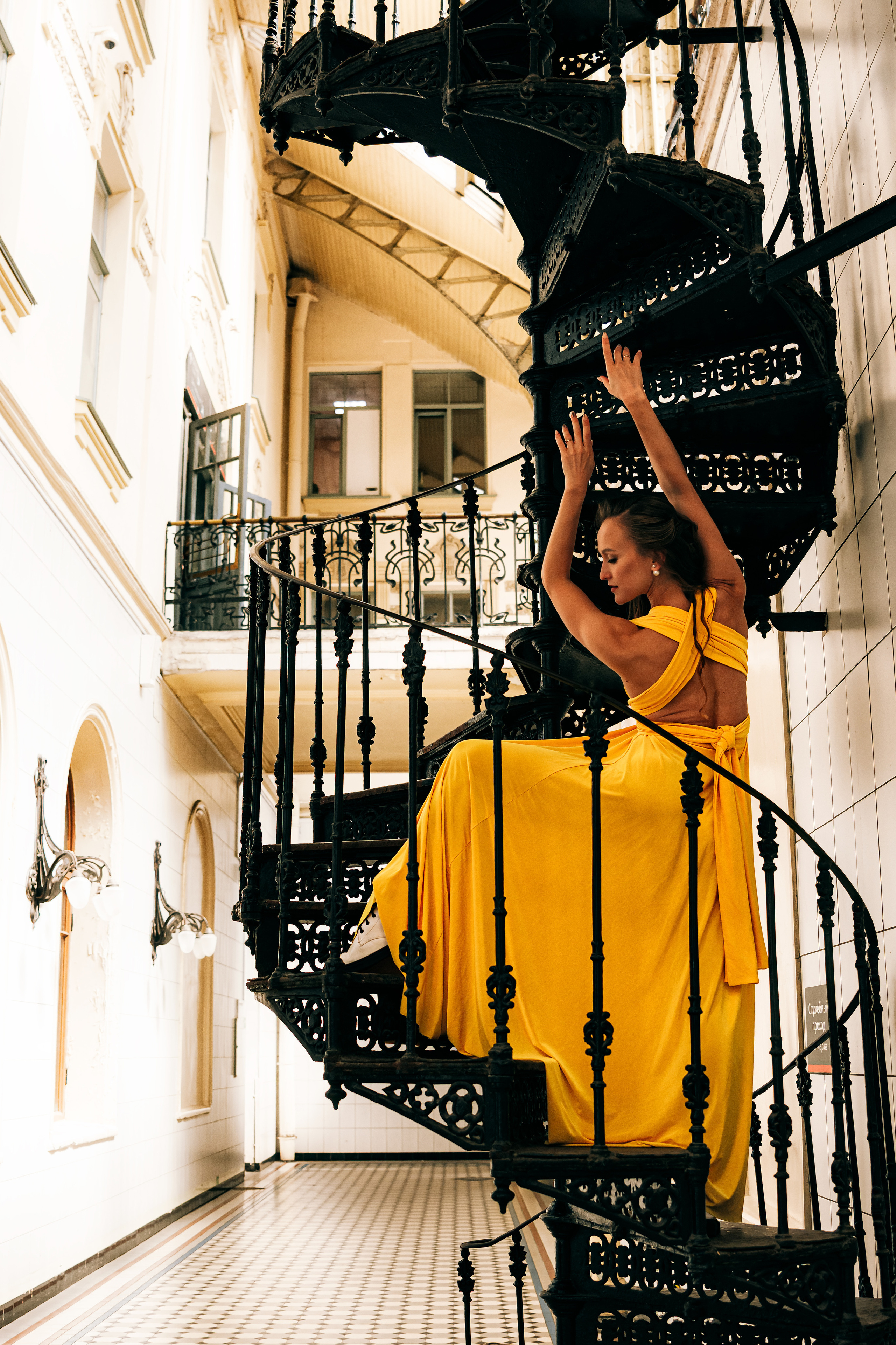 Молодая женщина, одетая в яркое желтое платье, танцует на Витебском вокзале.