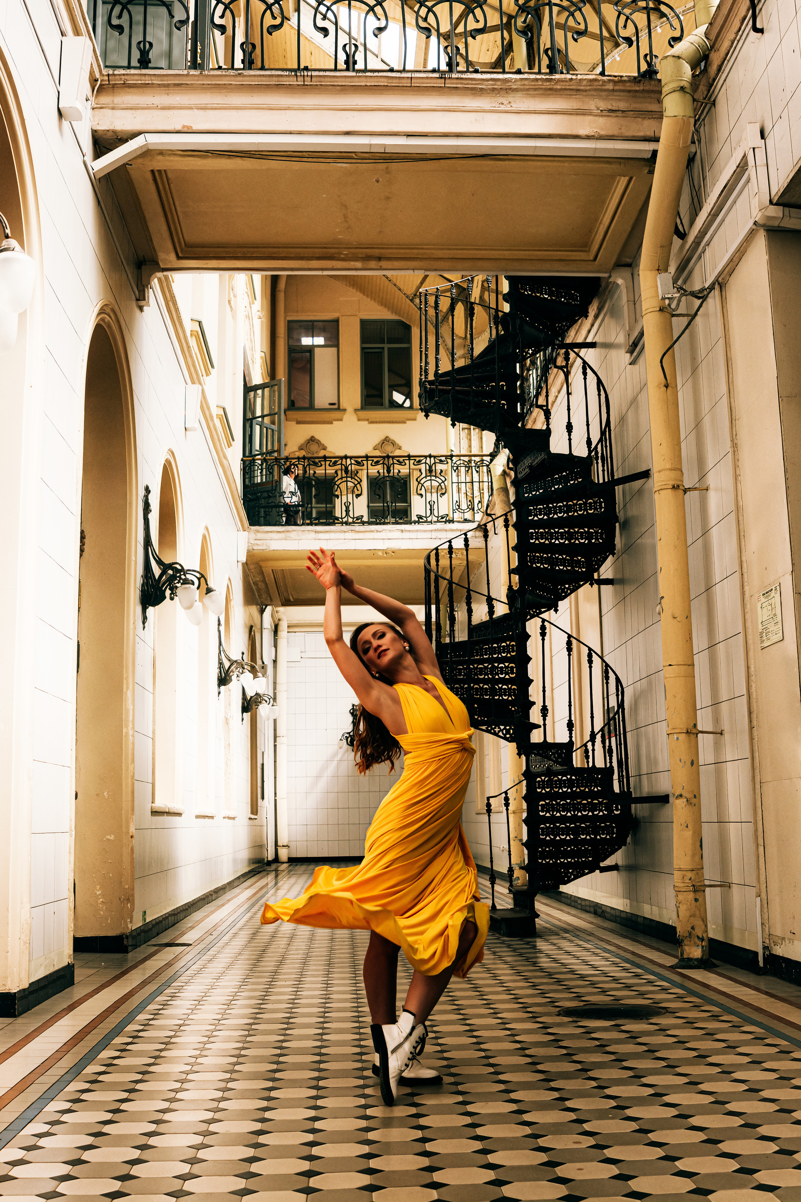Молодая женщина, одетая в яркое желтое платье, танцует на Витебском вокзале.