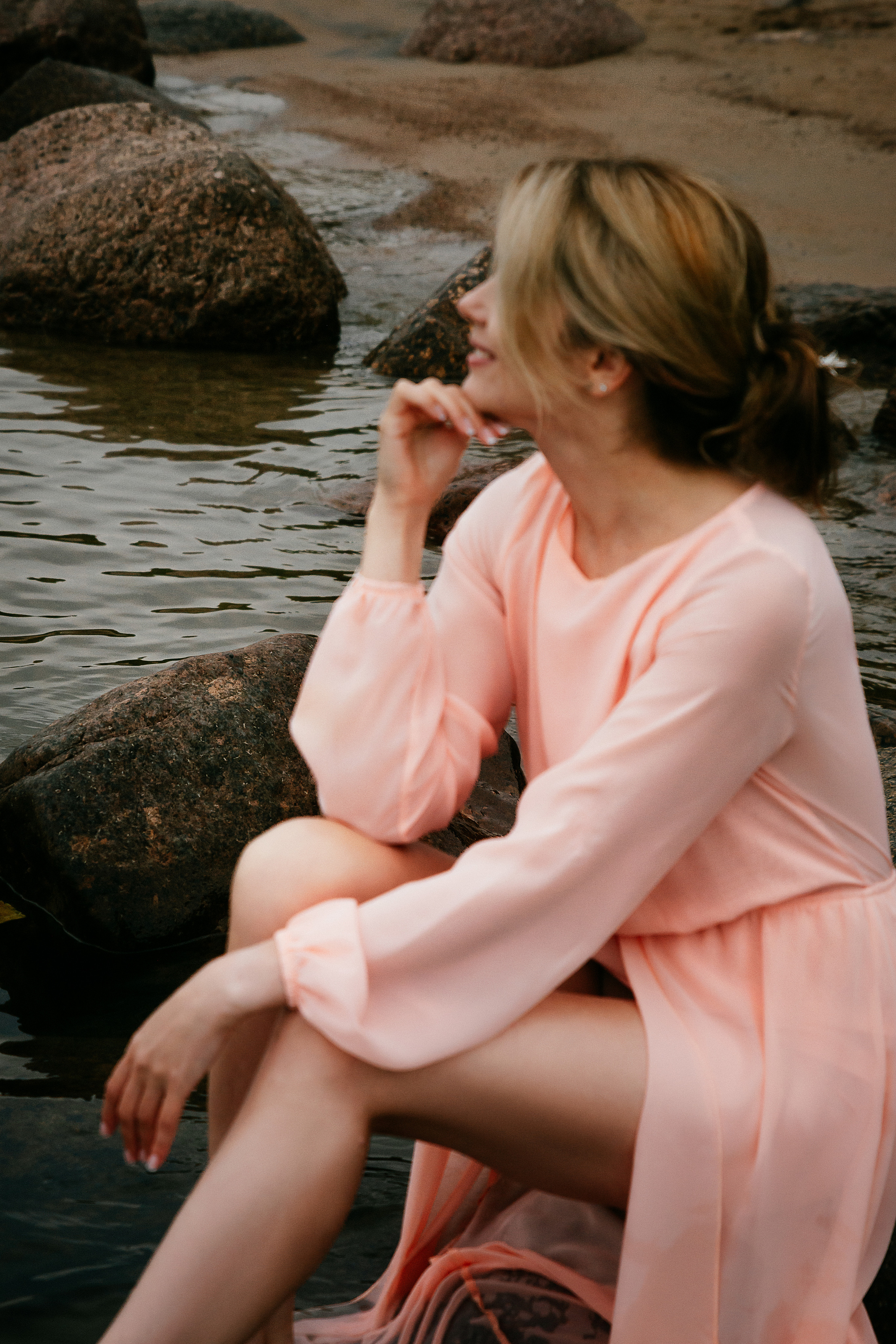 Одетая в легкое розовое платье, девушка создает гармоничное единство с окружающими ее камнями и водой.