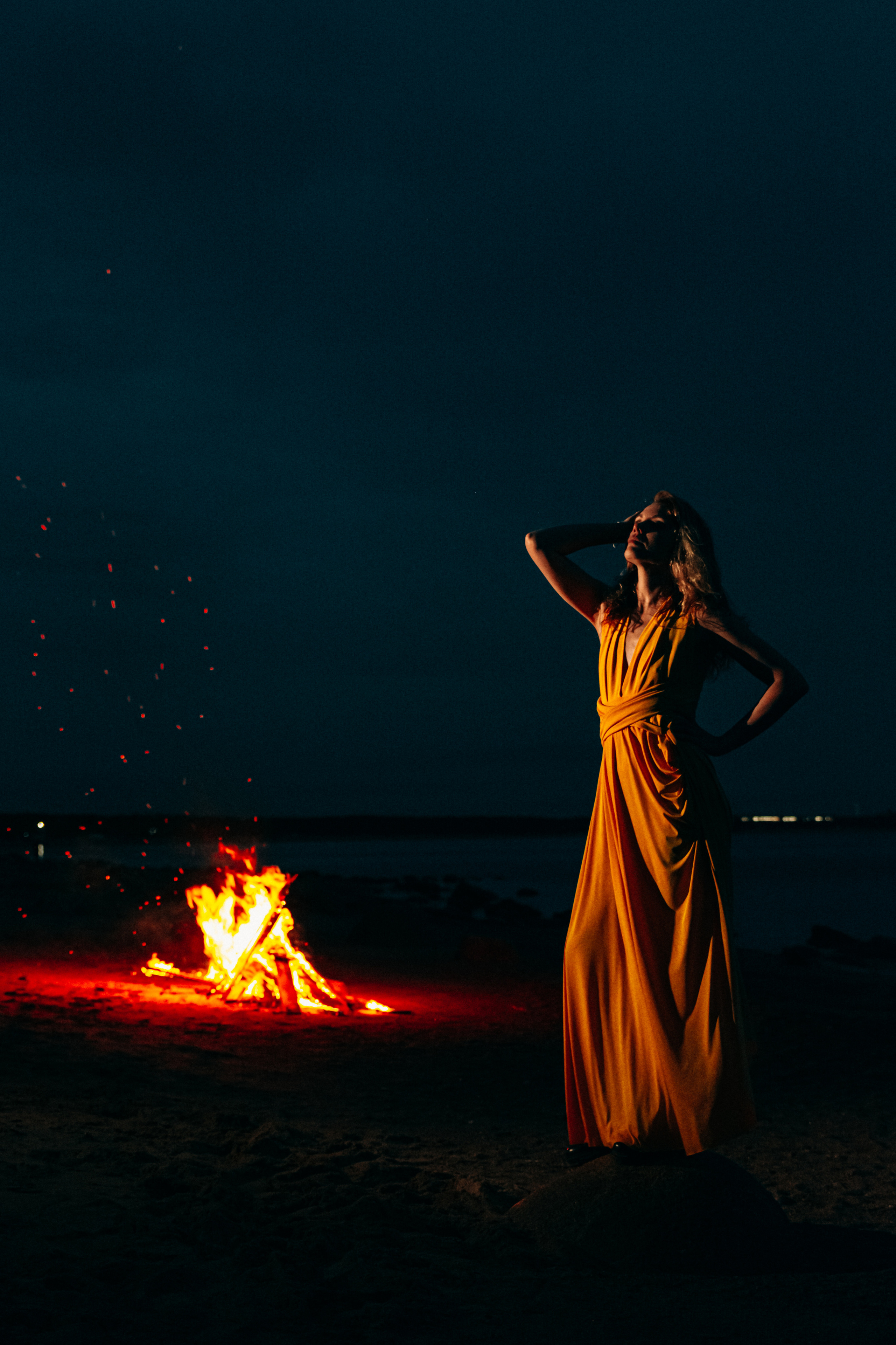  Фотография показывает девушку в желтом платье, ее силуэт подсвечен теплым светом костра, создавая прекрасное сочетание красоты и атмосферы.