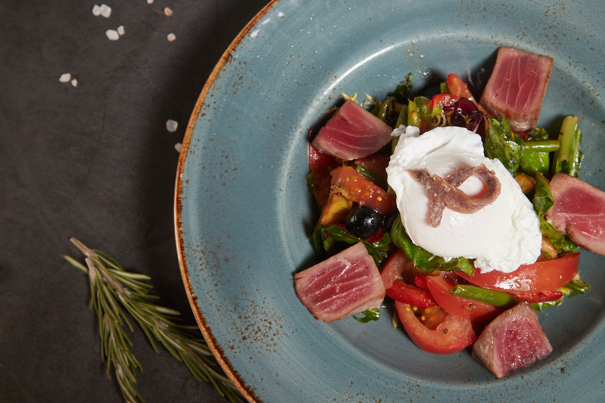 Фуд-фотография салата с сыром и овощами в голубой тарелке.