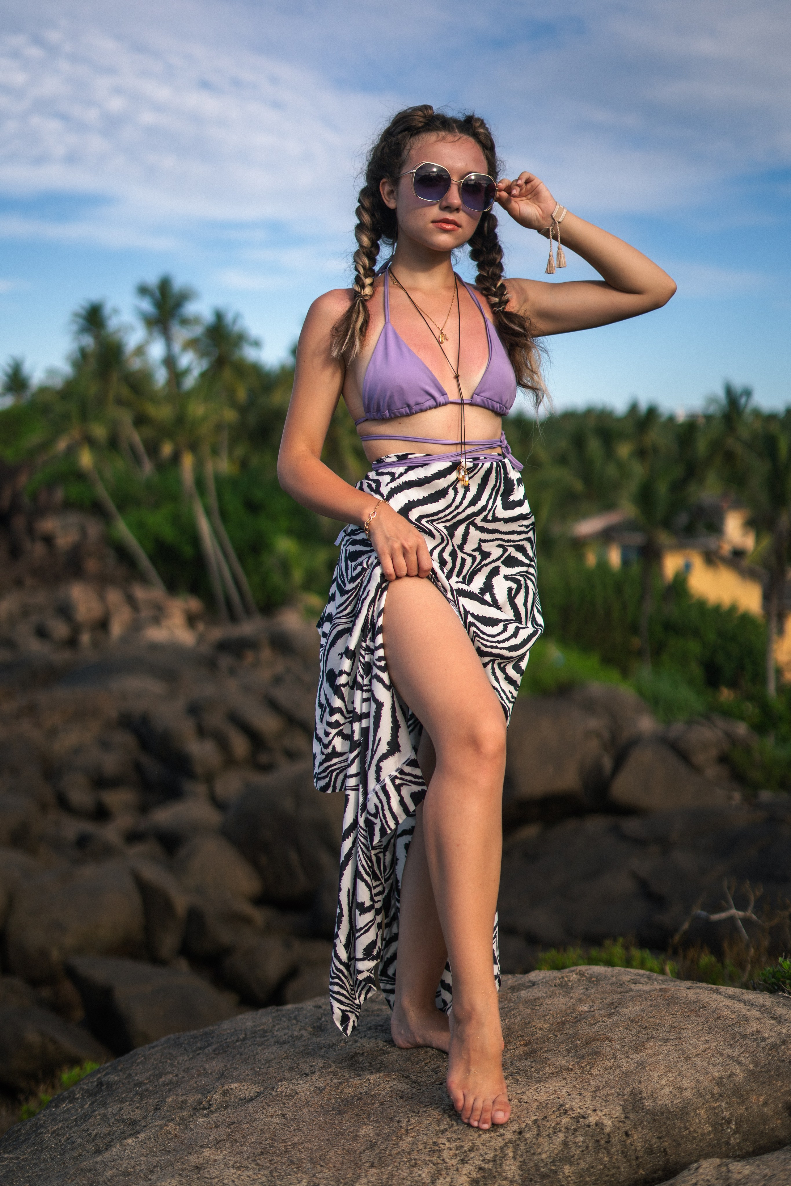 a young girl in a purple swimsuit posing on the rocks by the ocean