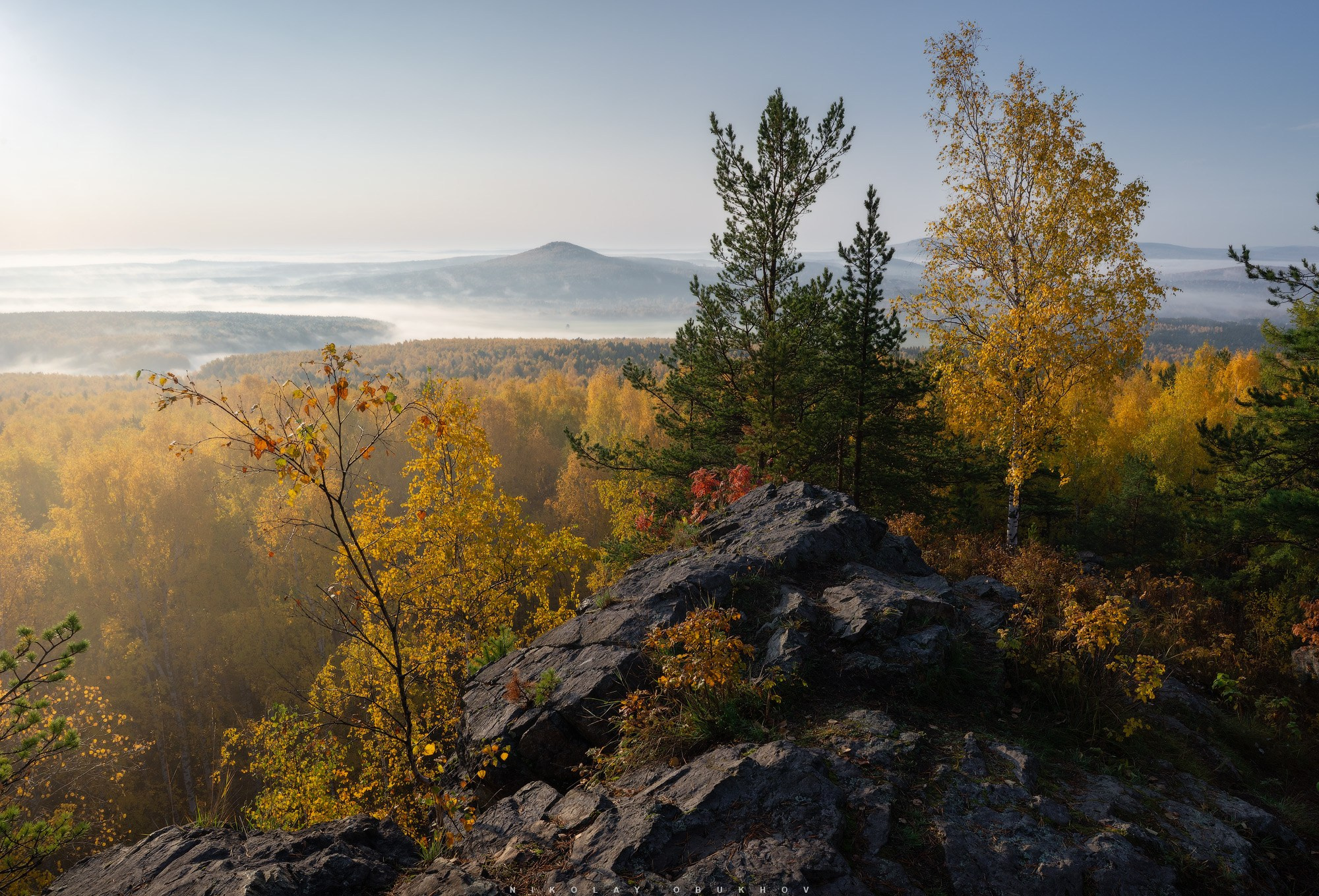 Одна из вершин Уральских гор, виден осенний лес и гора в тумане.