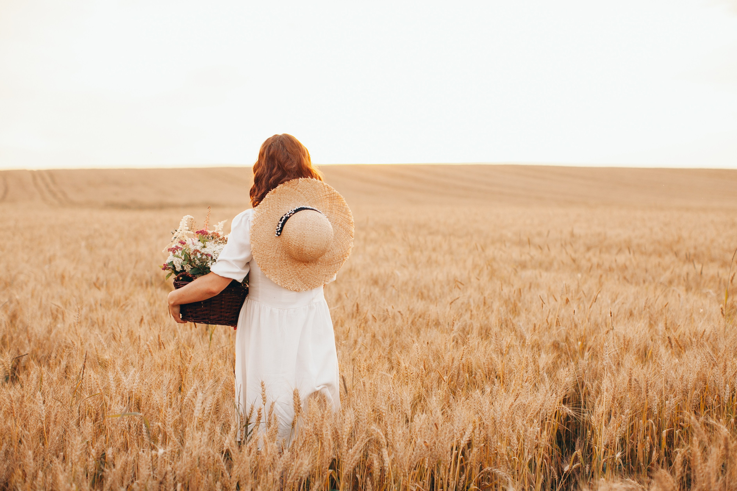 Фотография девушки со спины с корзиной и шляпой в поле на закате