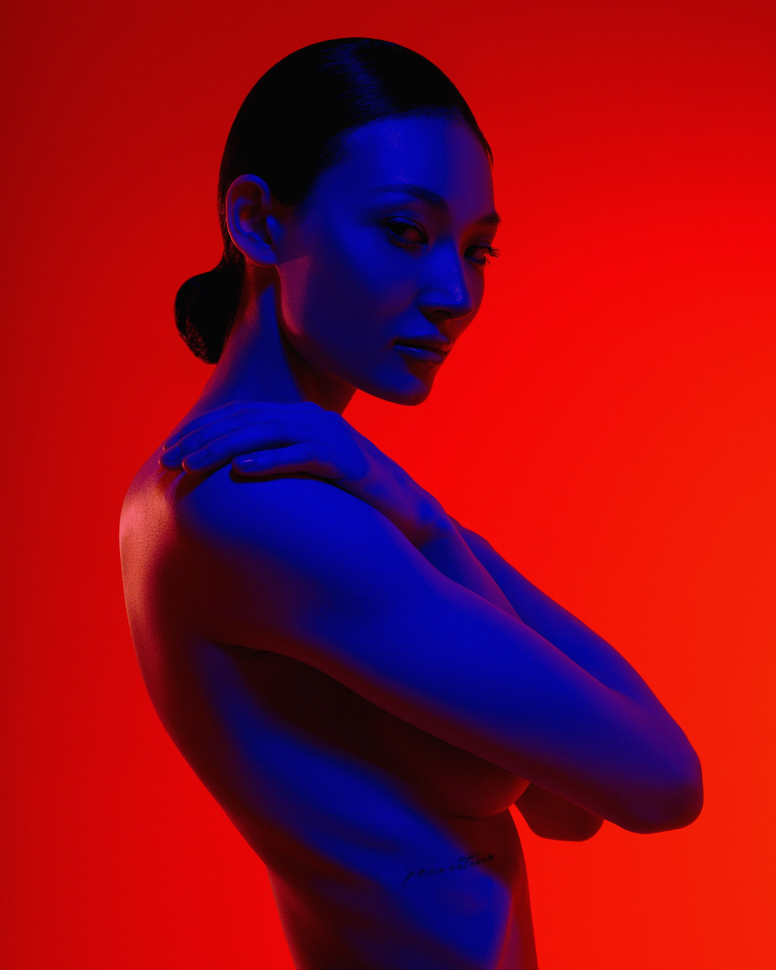 Фэшн фотография с обнажённой девушкой азиатской внешности на красном фоне, залитая синим светом
