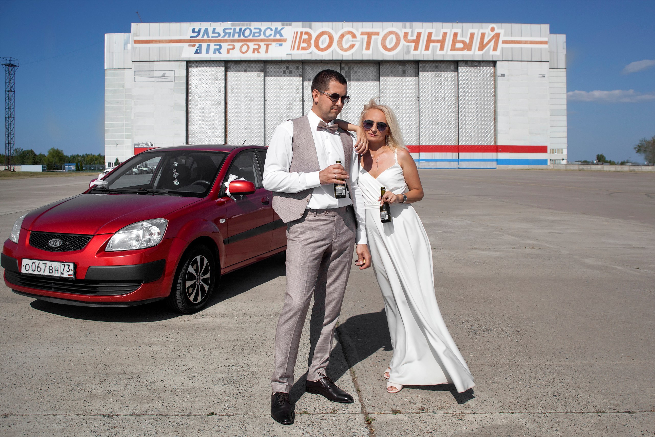 Невеста опирается на жениха на фоне красной машины в аэропорту Восточный, свадебная прогулка Ульяновск