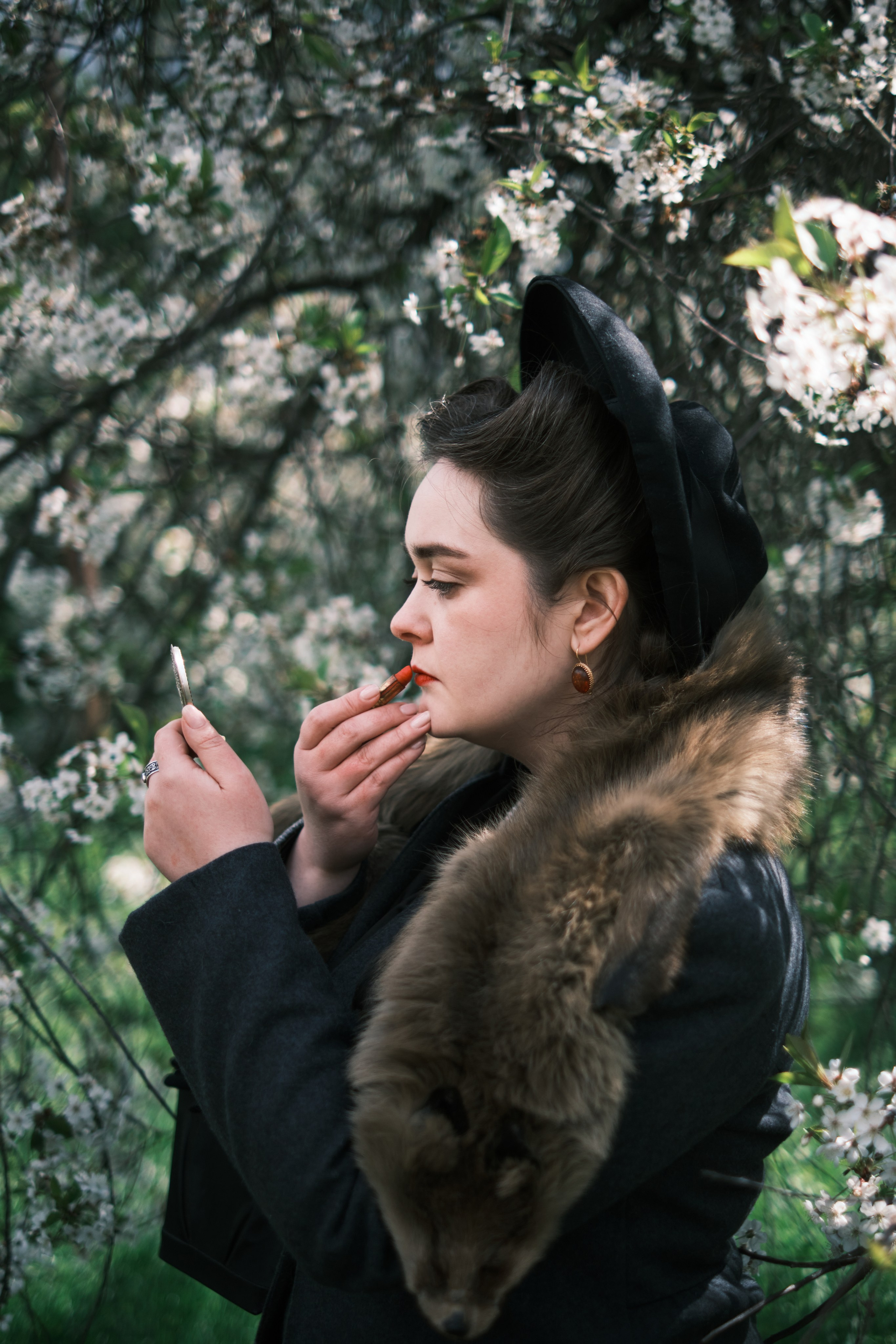 Девушка в старинном наряде и шляпе красит губы