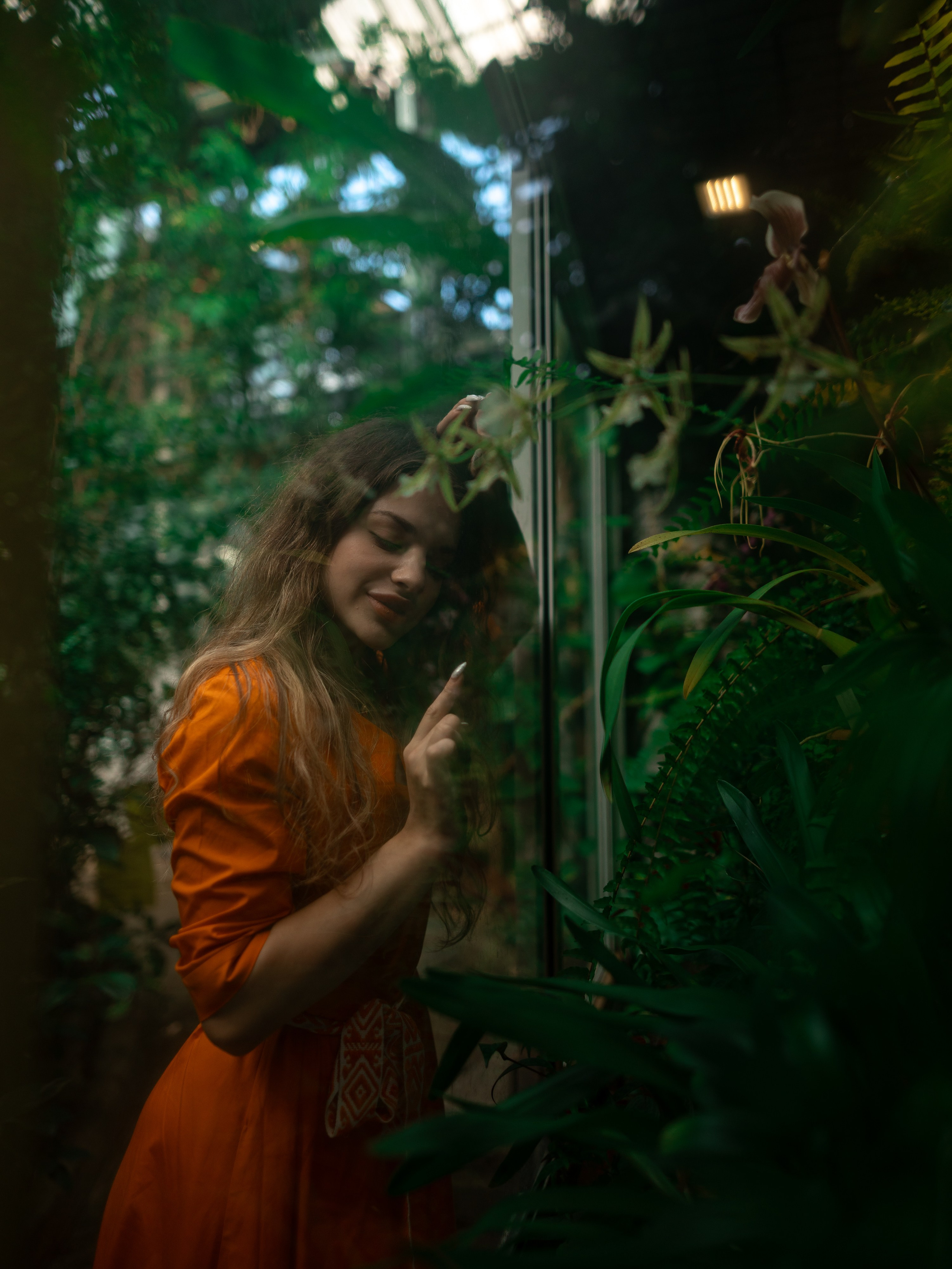 Девушка в оранжевом платье стоит на фоне зелени