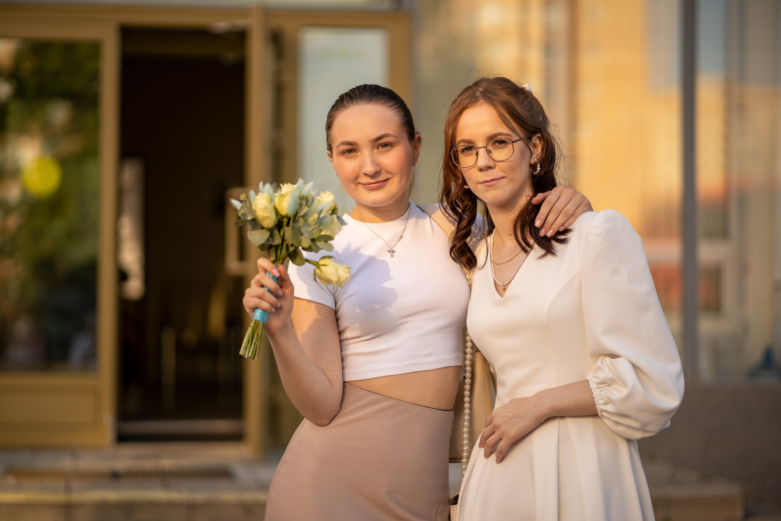 Невеста с подругой стоят у загса со свадебным букетом 