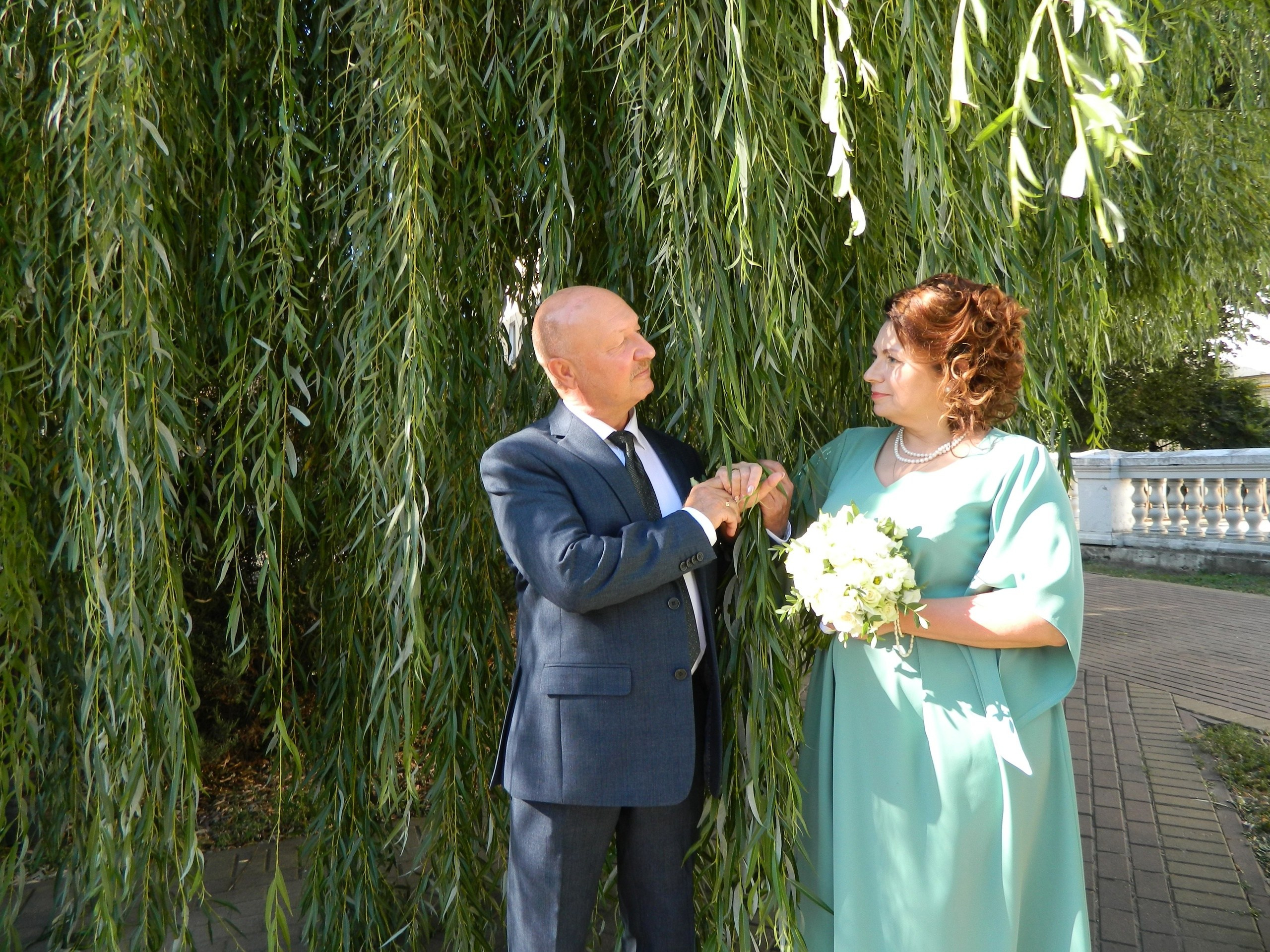 супруги вышли из ЗАГСа и любуются друг другом на фоне деревьев