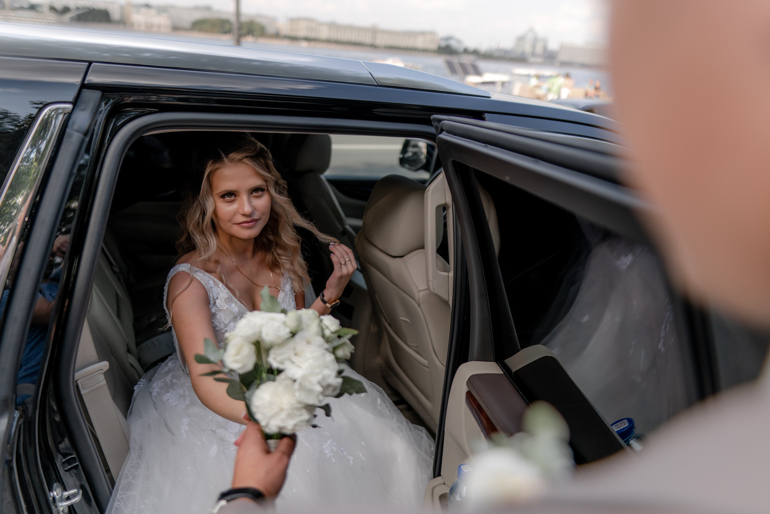 Невеста с букетом цветов выходит из черной машины