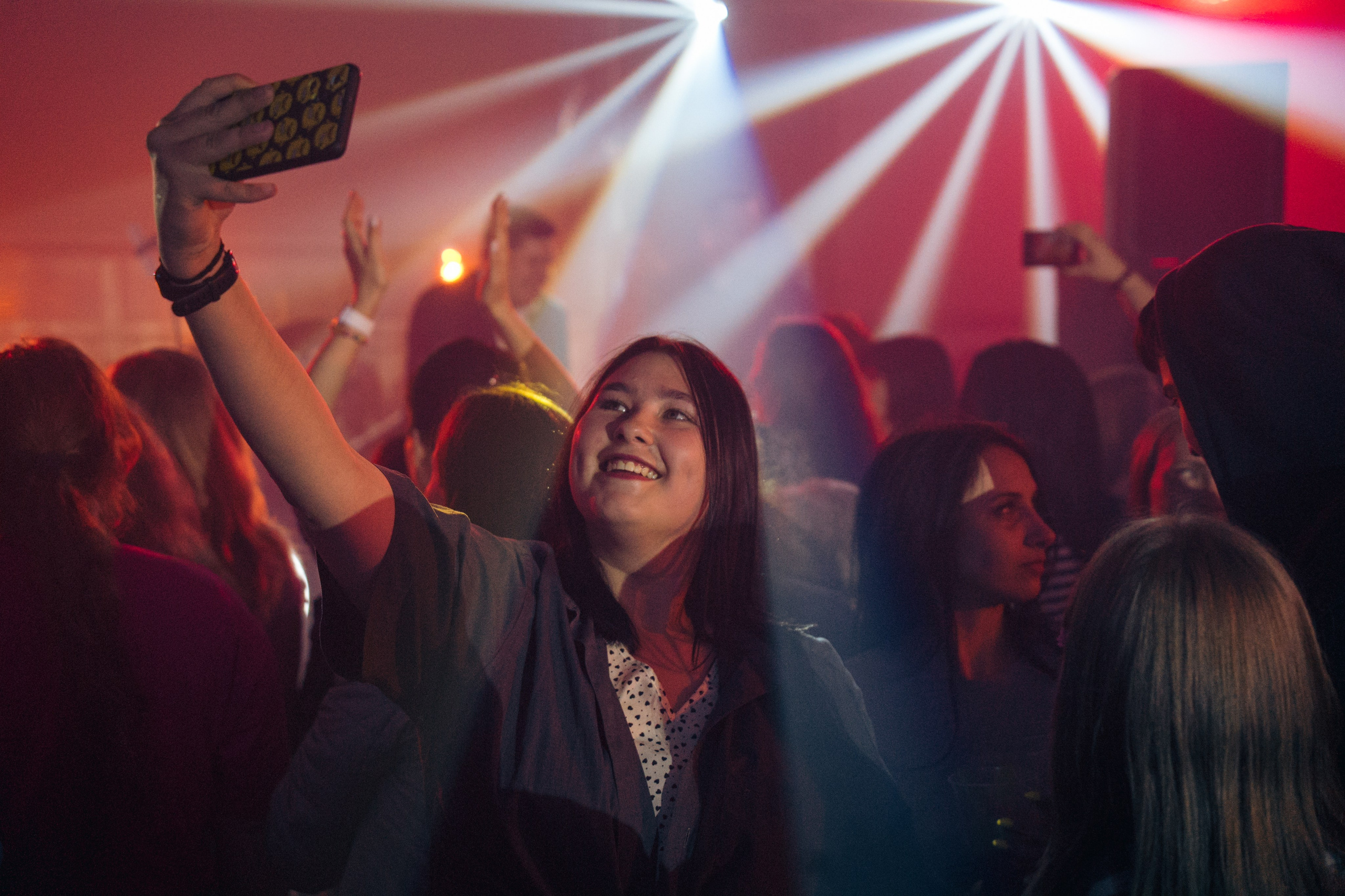 Девушка делает селфи на фоне танцующей толпы с яркими световыми лучами