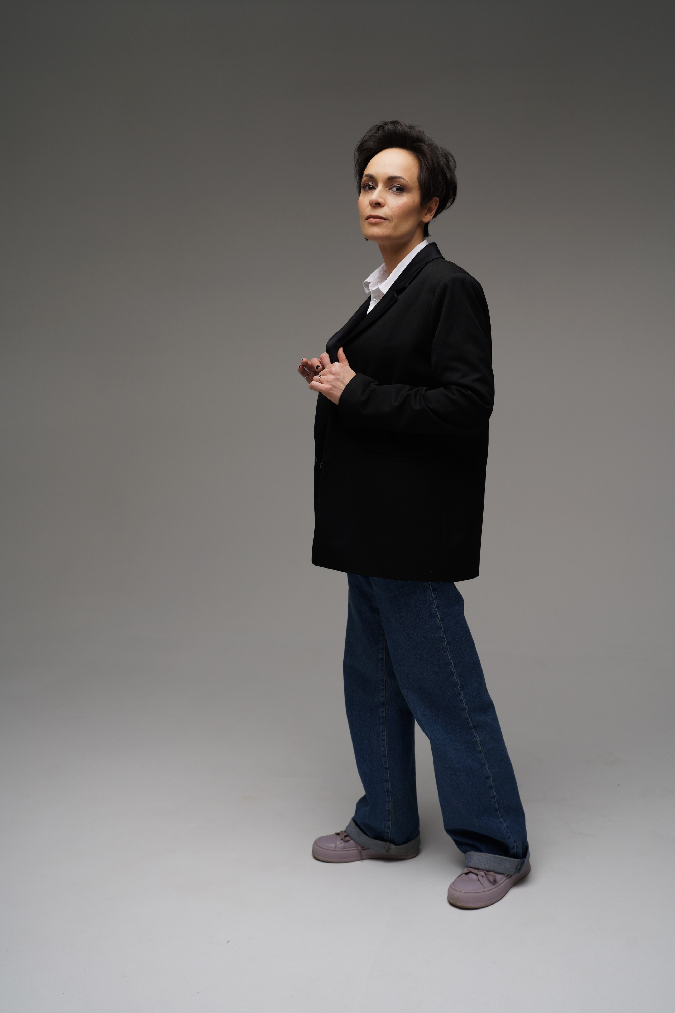 Девушка в пиджаке на циклораме позирует держа руками края пиджака 