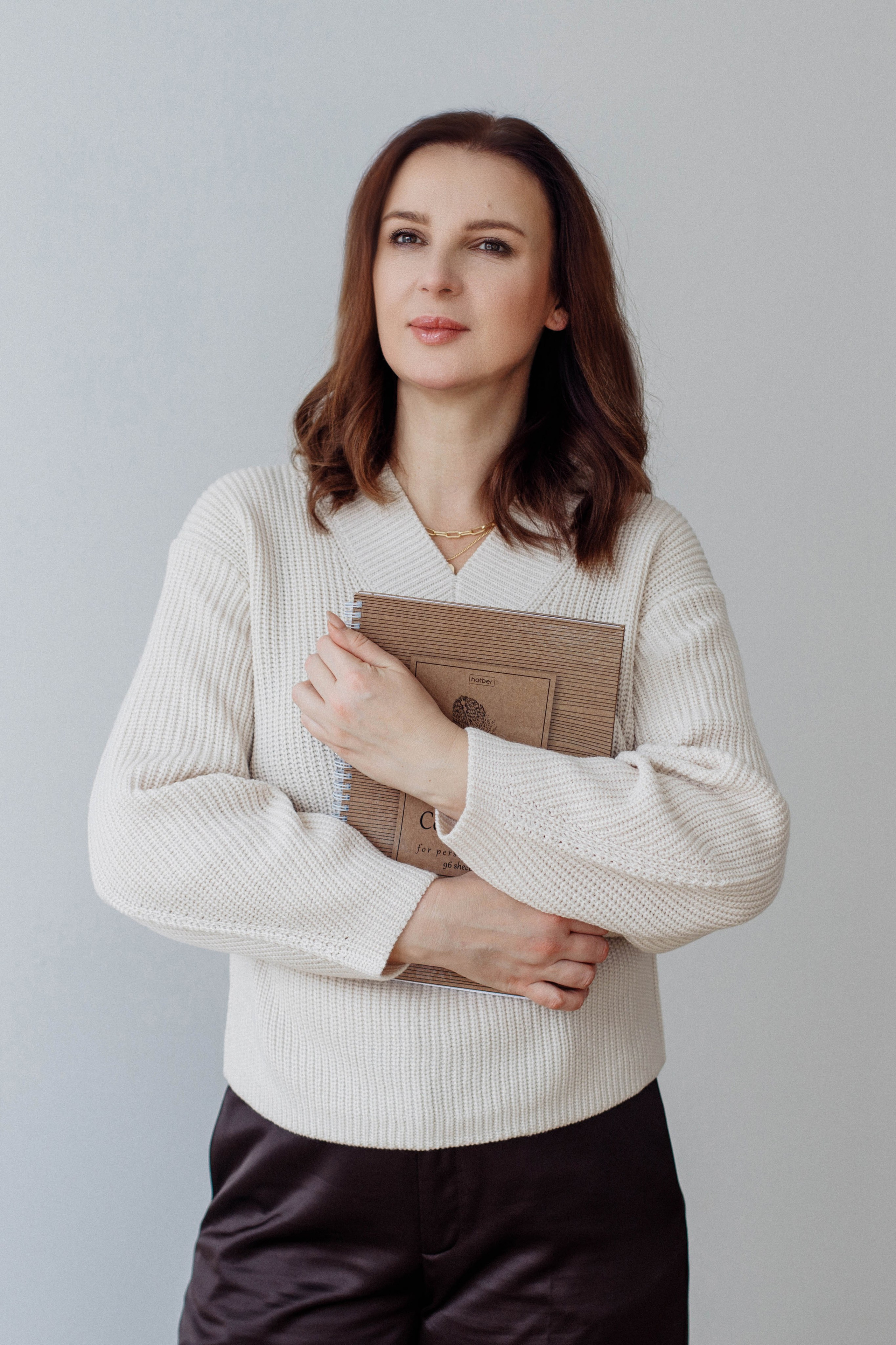 Созерцательный кадр: психолог, прижав к себе книгу, стоит у стены и смотрит в окно. Образ глубокого размышления.