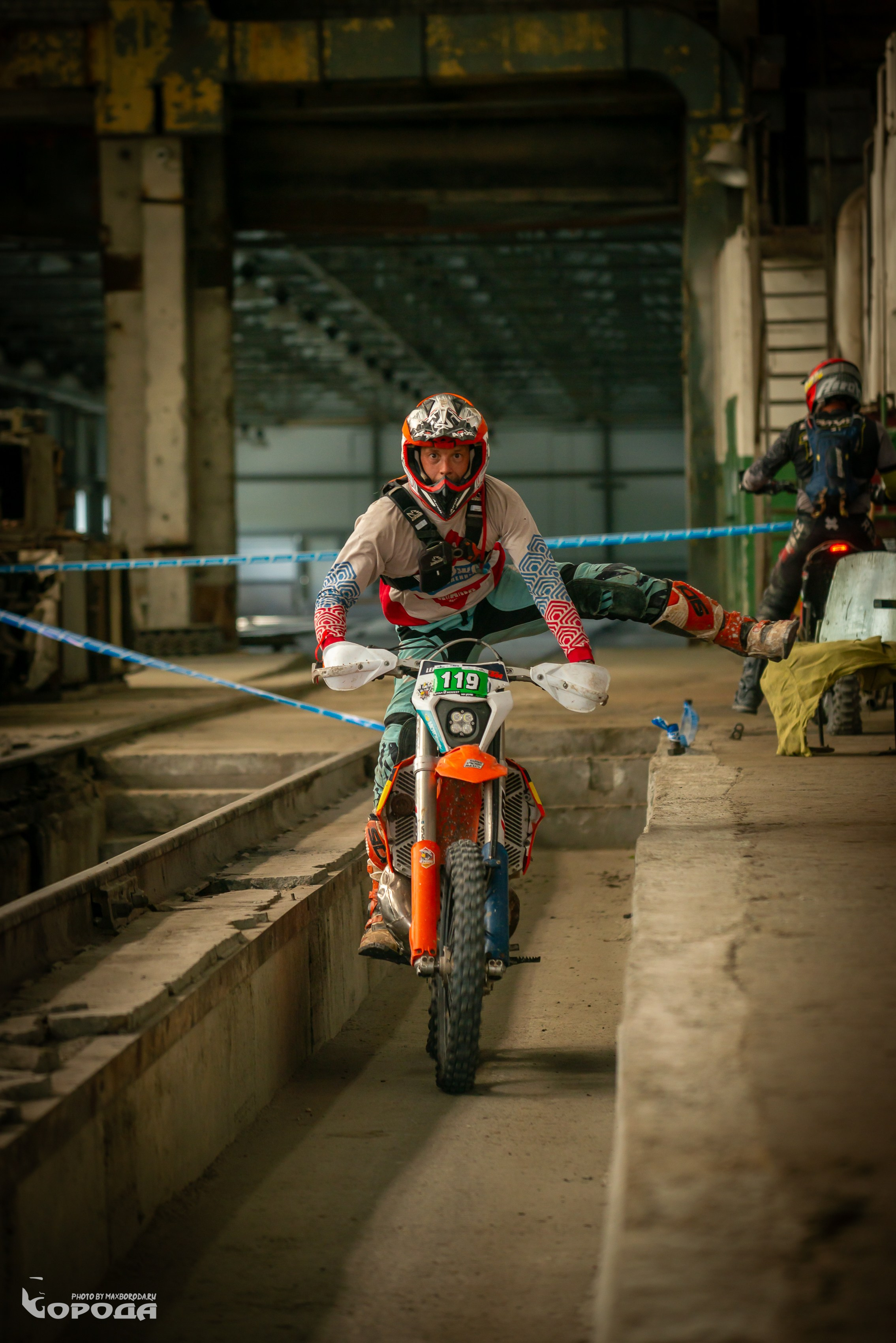 Эндуро-спортсмен в полной экипировке преодолевает препятствие в антураже завода.