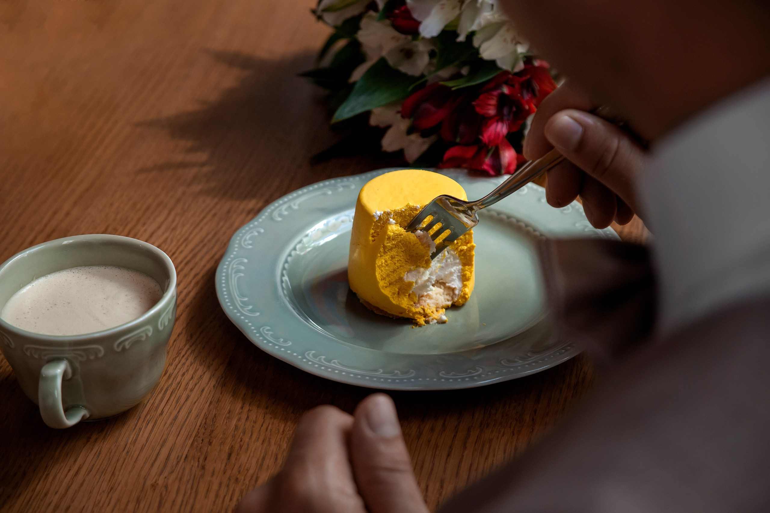 Фотосъёмка деталей, десерт желтого цвета на тарелке и чашка кофе в глиняной чашке