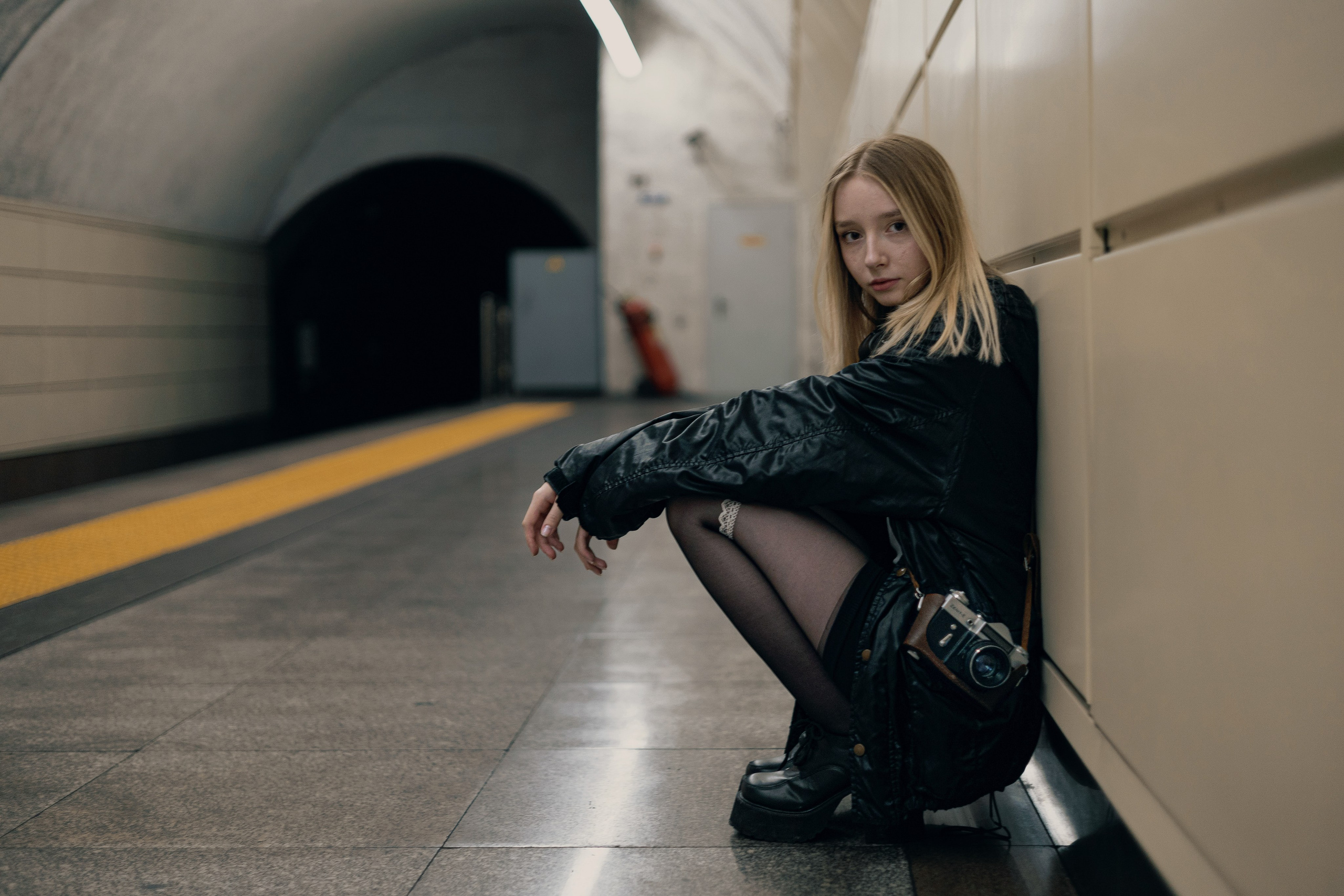 Модель в стиле гранж сидит у стены тоннеля метро, задумчивая атмосфера