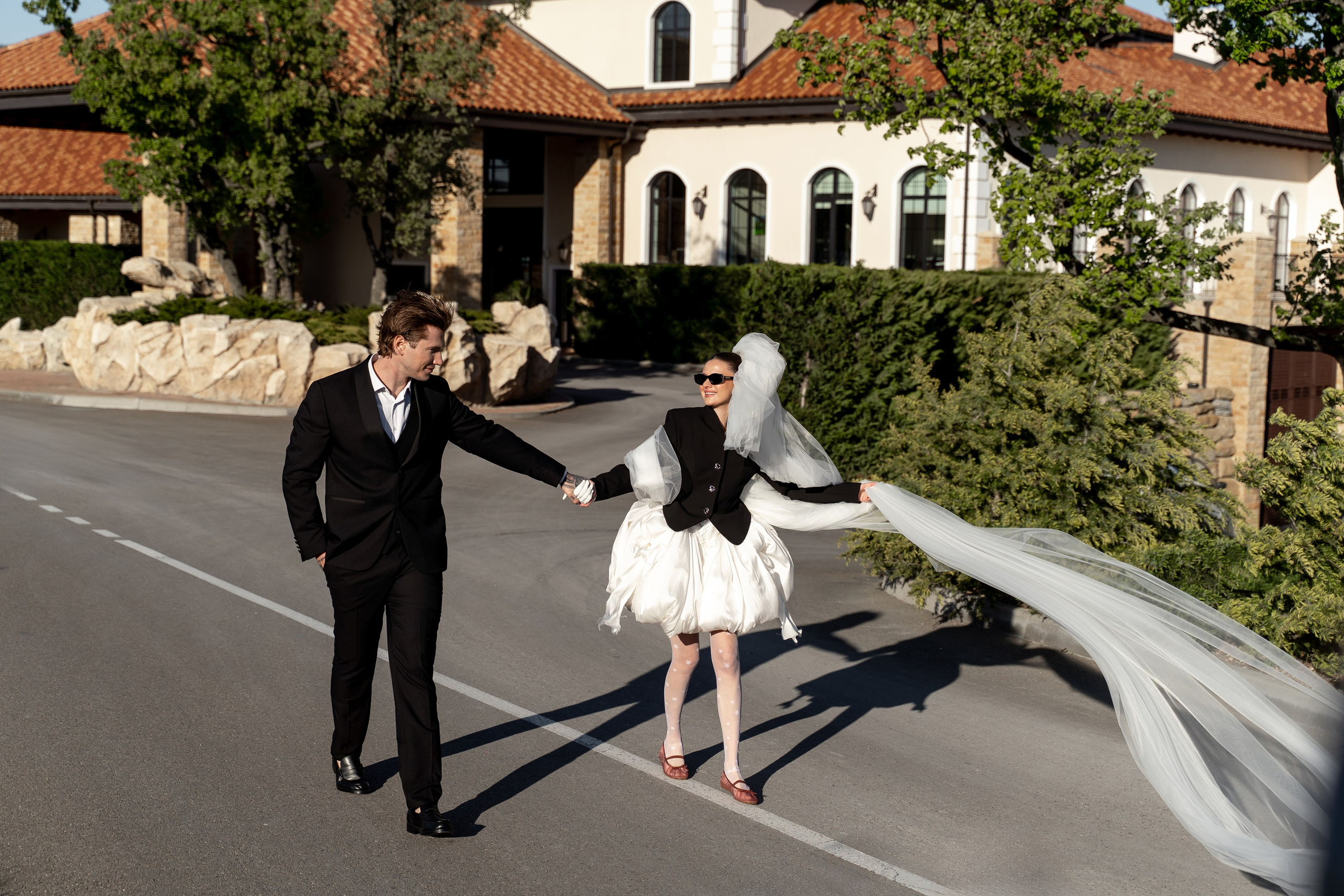 Невеста и жених смеются, держась за руки во время свадебной съемки в гольф-клубе Геленджика