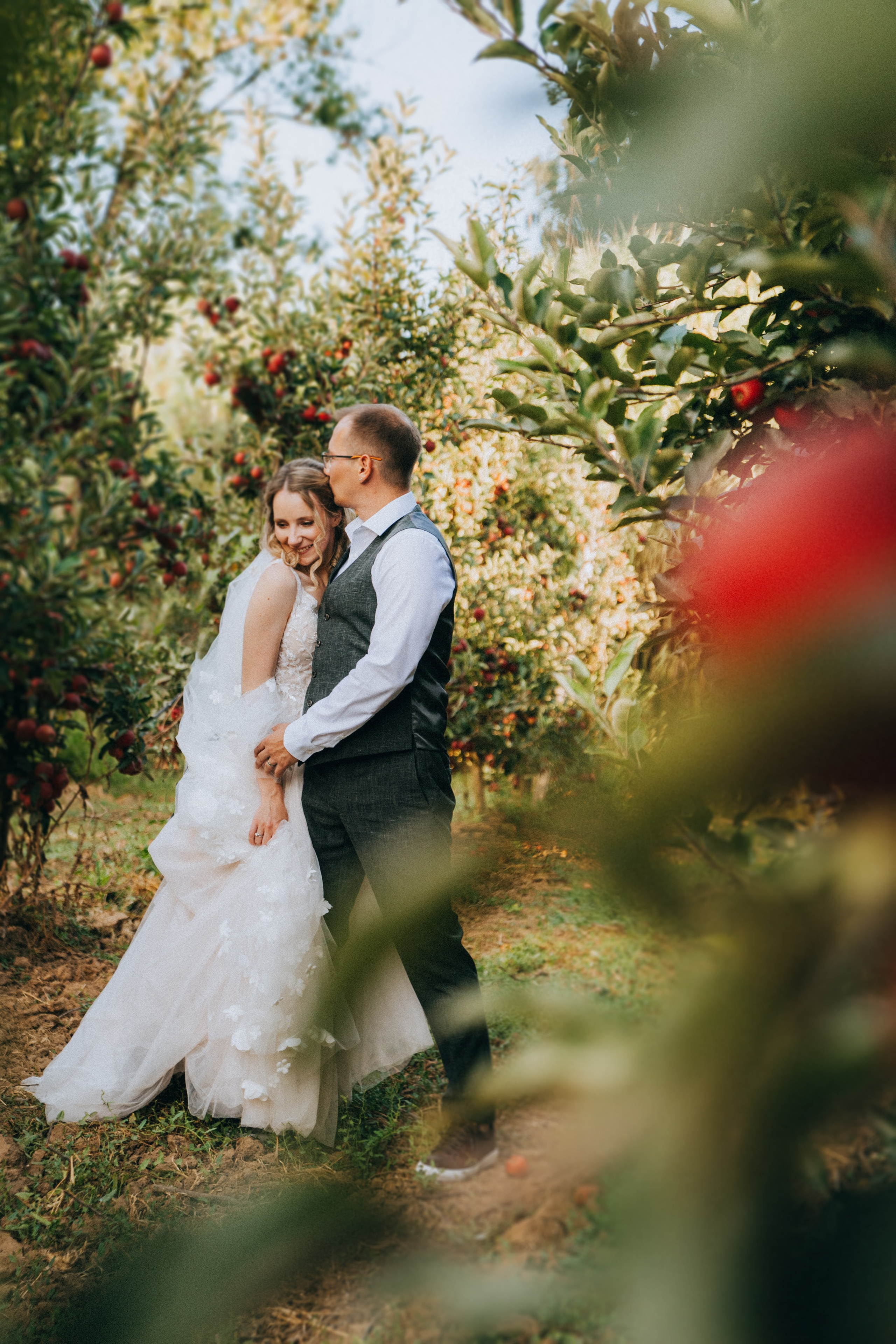 Жених и невеста обнимаются среди яблоневого сада, вокруг созревшие яблоки.