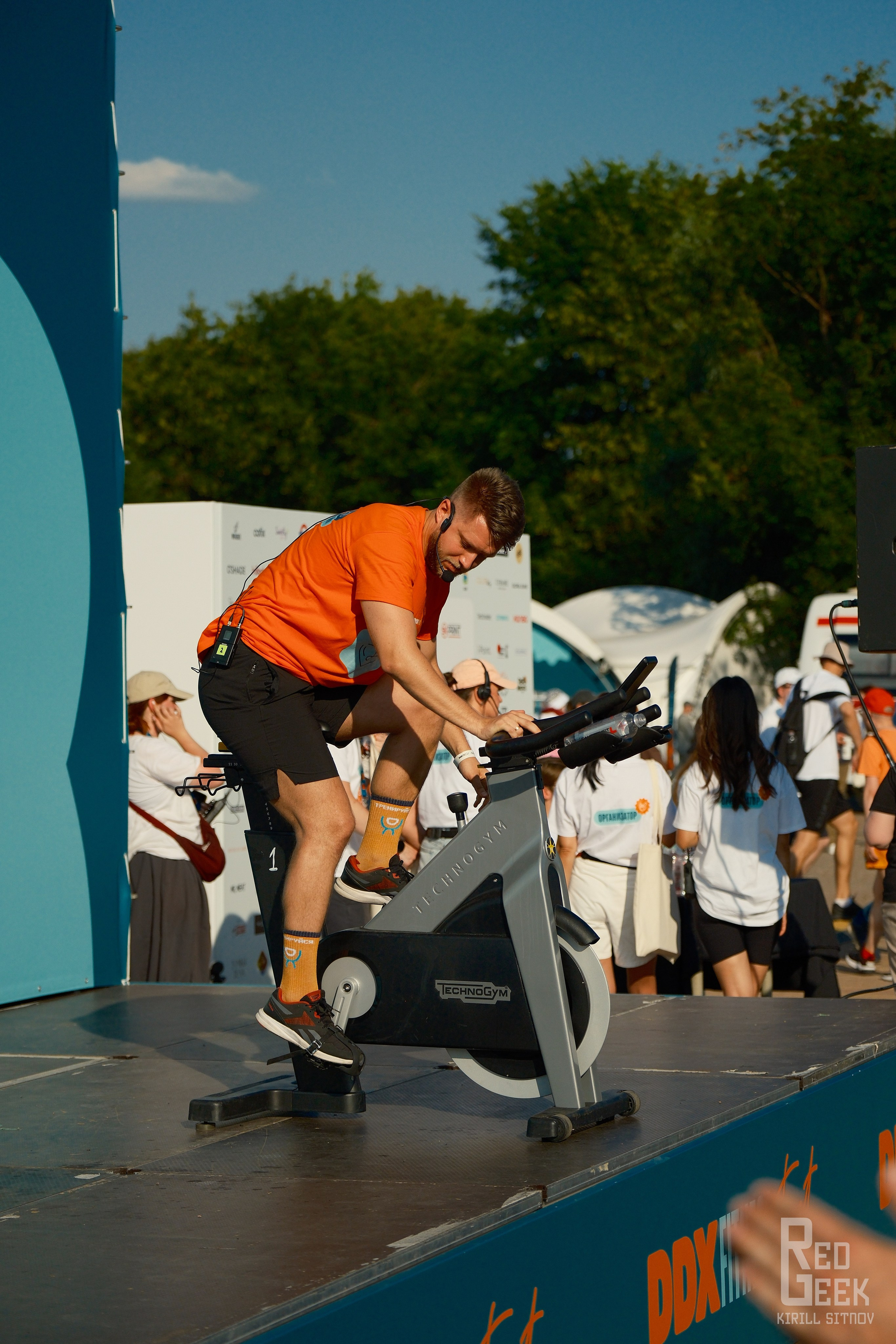 Тренер крутит велотренажёр на открытом воздухе фестиваля DDX Fitness.