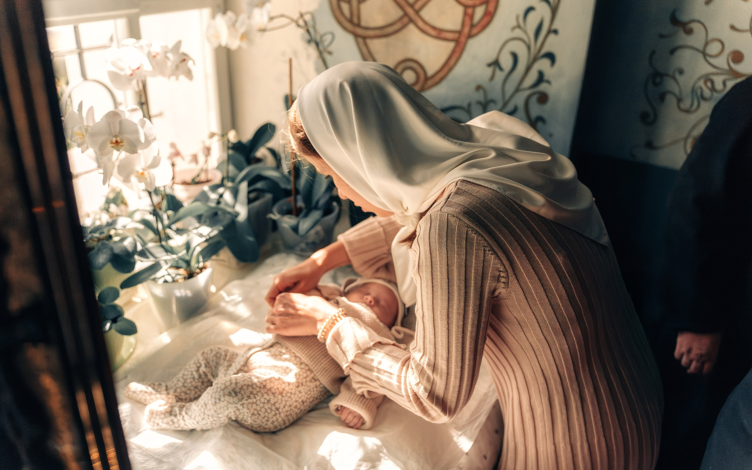 Мама раздевает малыша перед крещением.