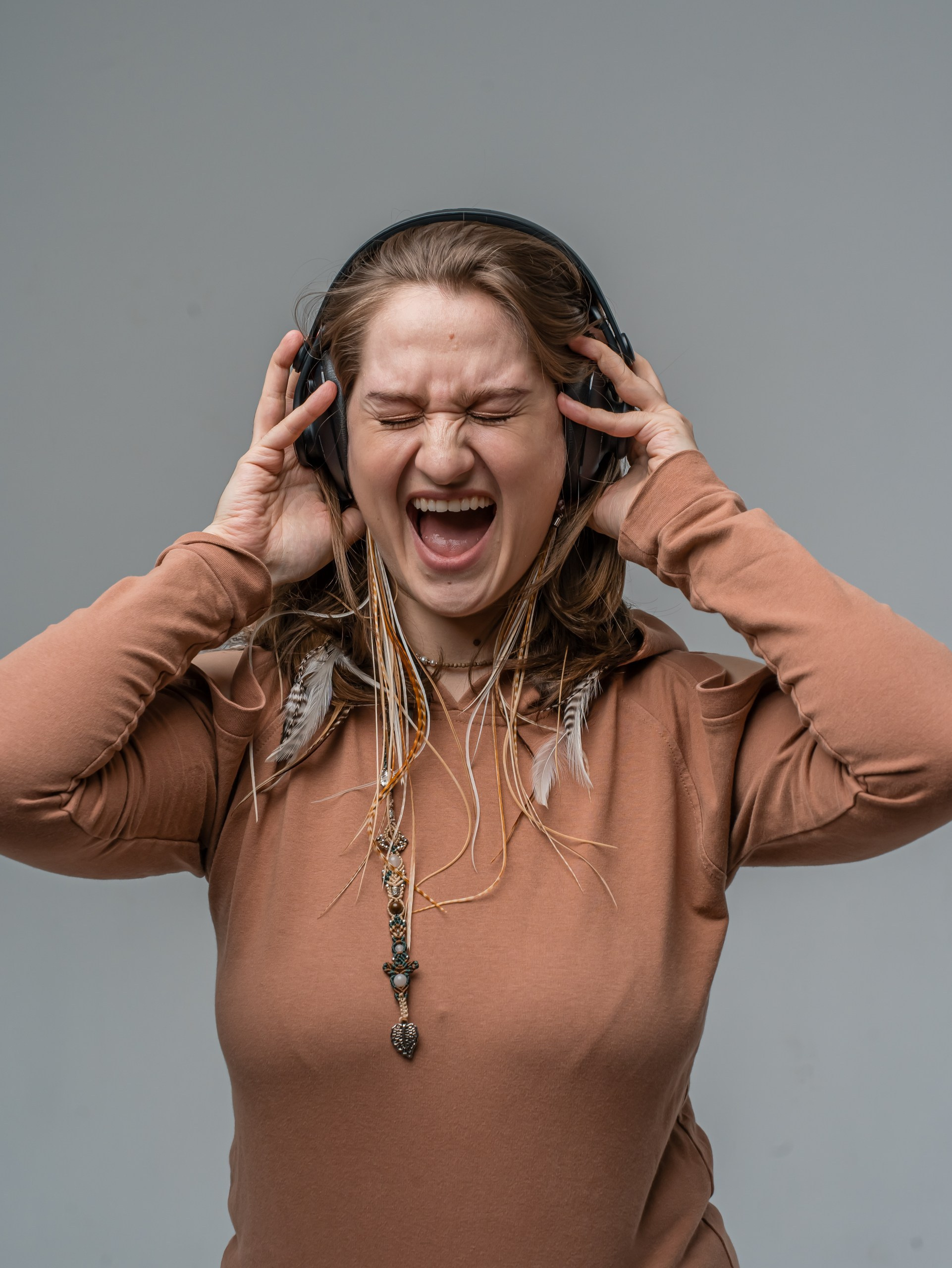 девушка в студии в наушниках, выражает эмоции радости, искусственный свет, серый фон
