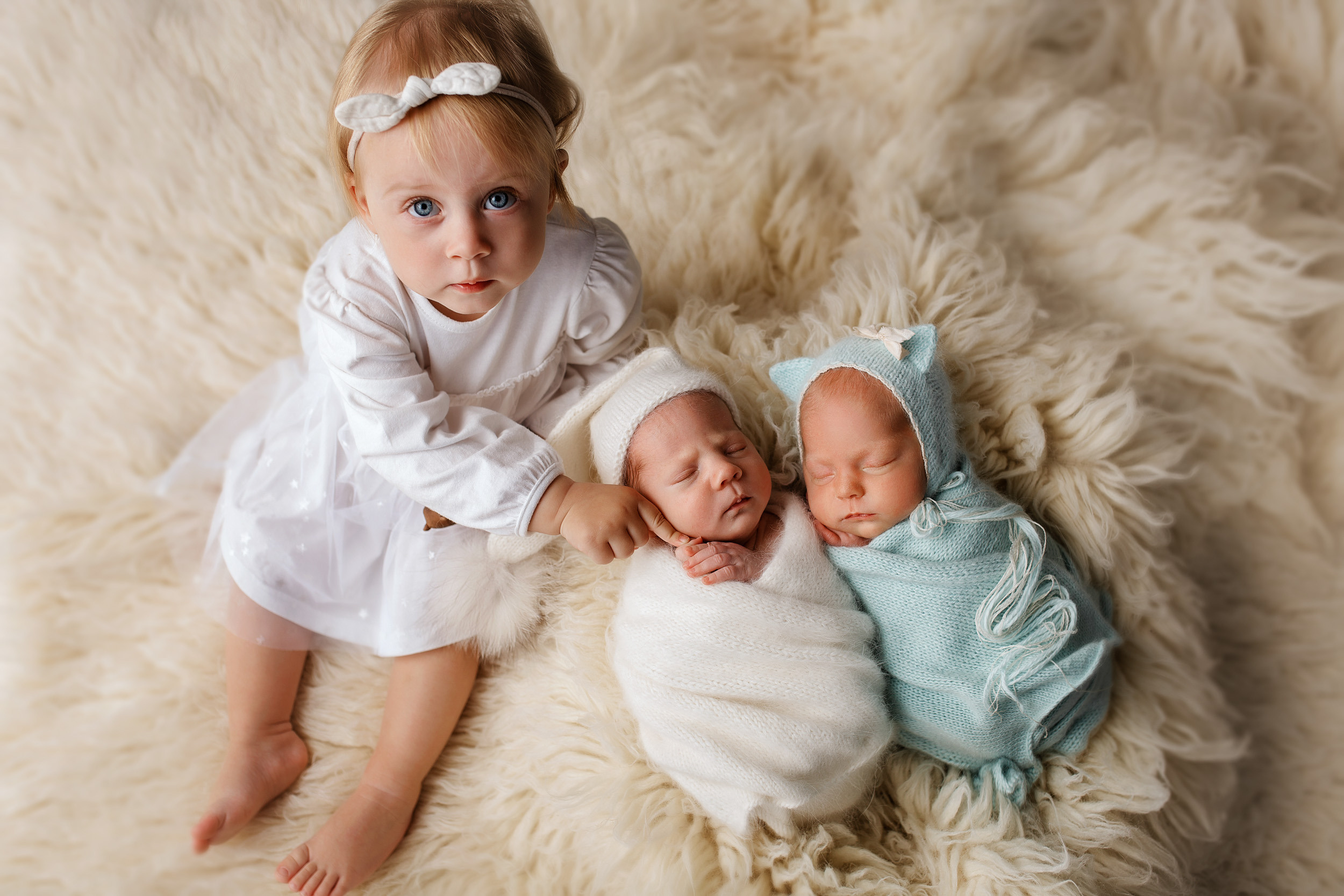 Сестричка с новорожденными двойняшками позирует сидя на фоне.