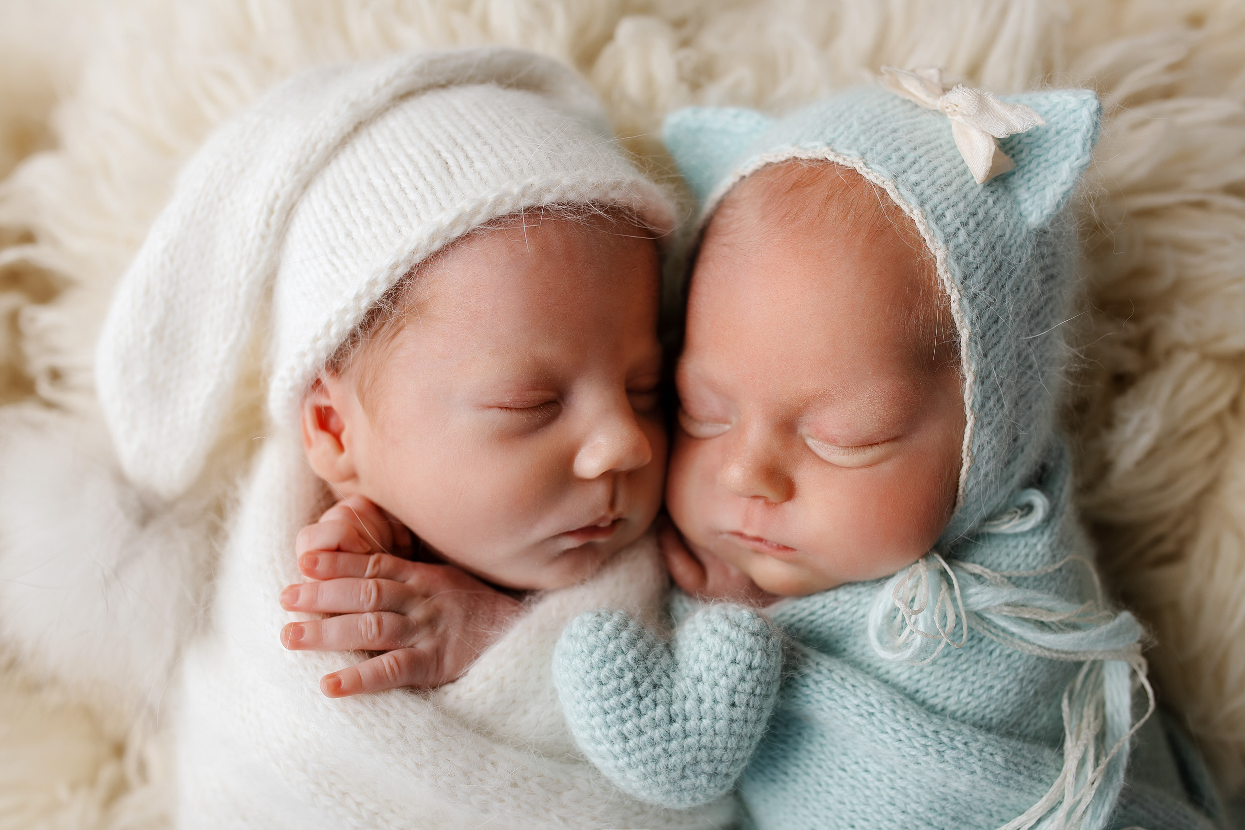 Новорожденные дети лежат на флокати с игрушкой и в милых шапочках. 