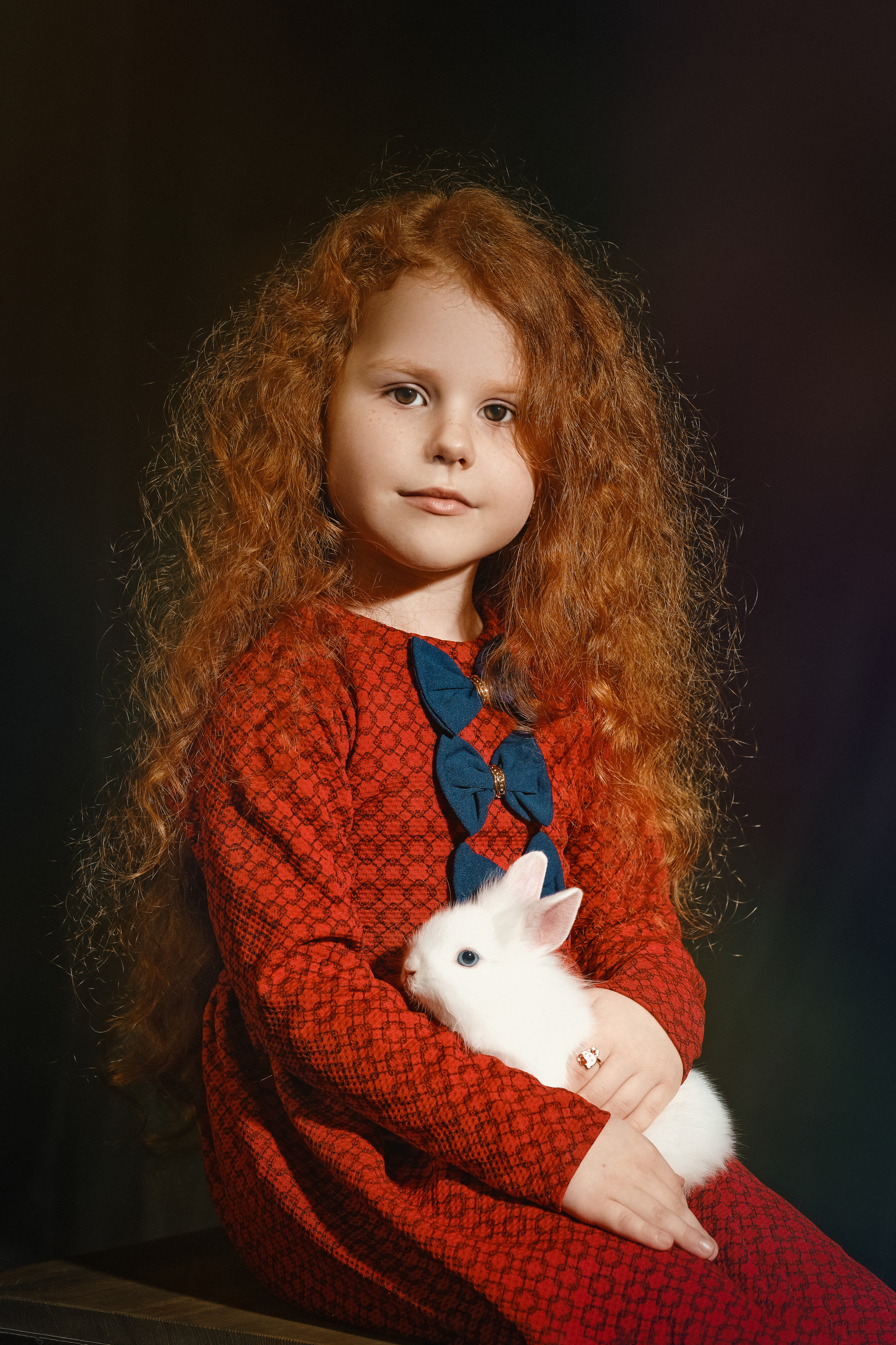 Девочка в красном платье и кроликом на коленях с кучерявыми рыжими волосами