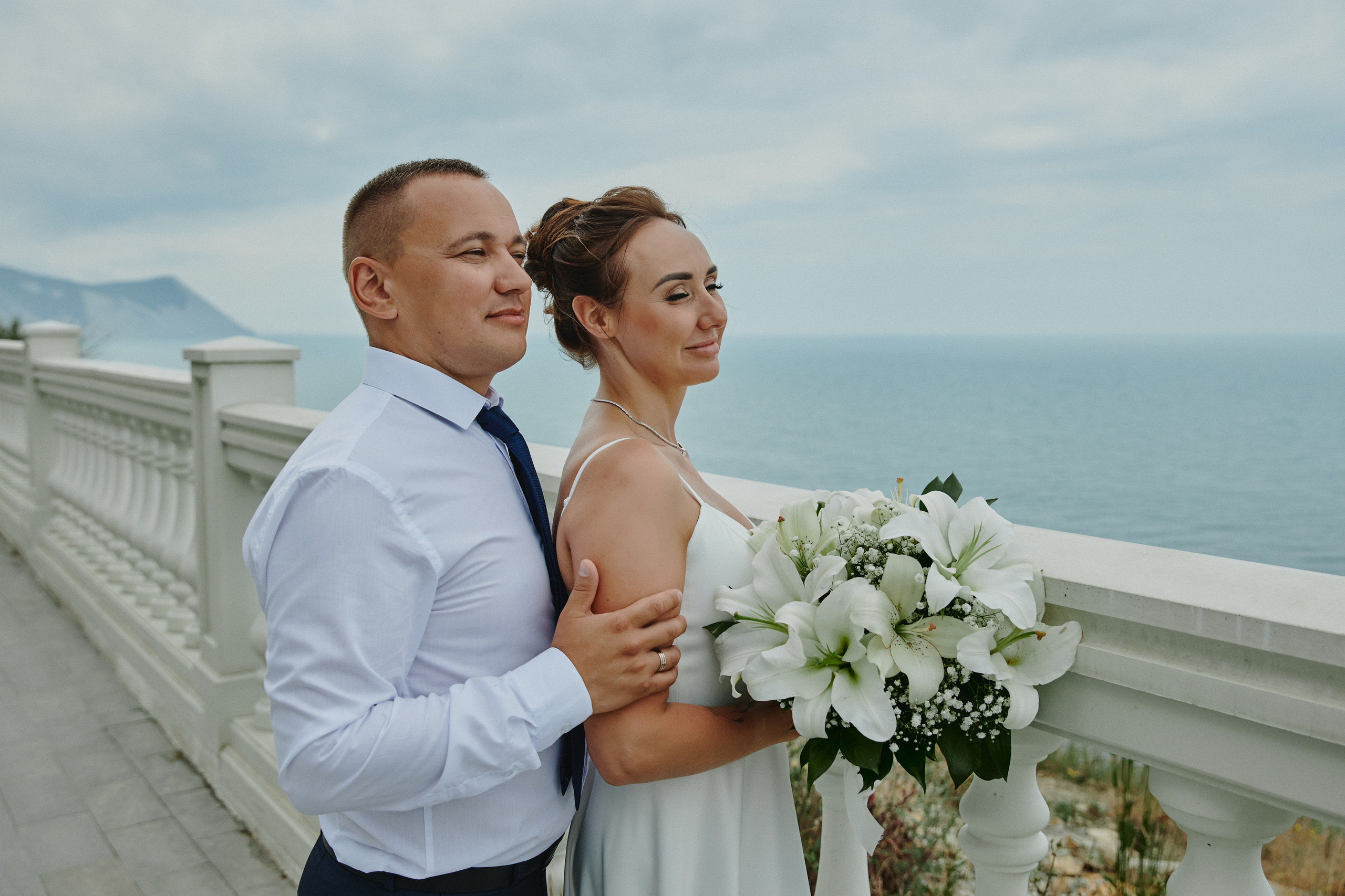 Жених обнимает невесту за плечи на набережной возле моря